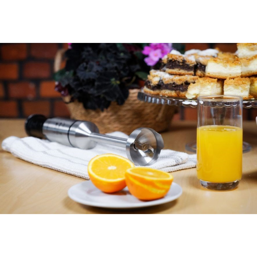 Blender ręczny obok pomarańczy i szklanki soku pomarańczowego.