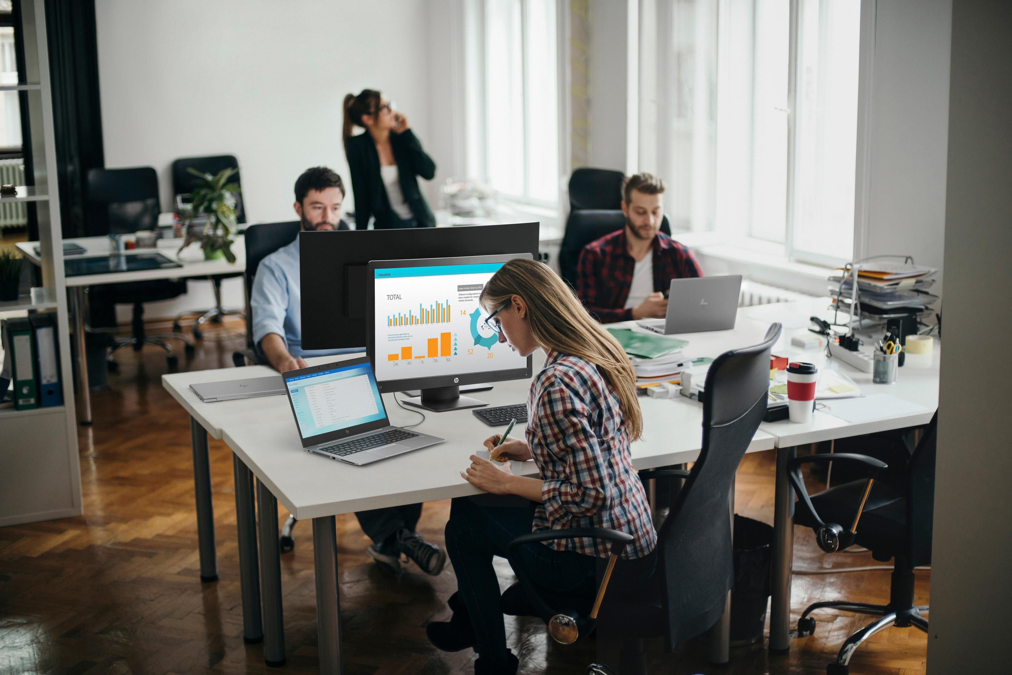 Escena de oficina con gente trabajando en computadoras y viendo gráficos.