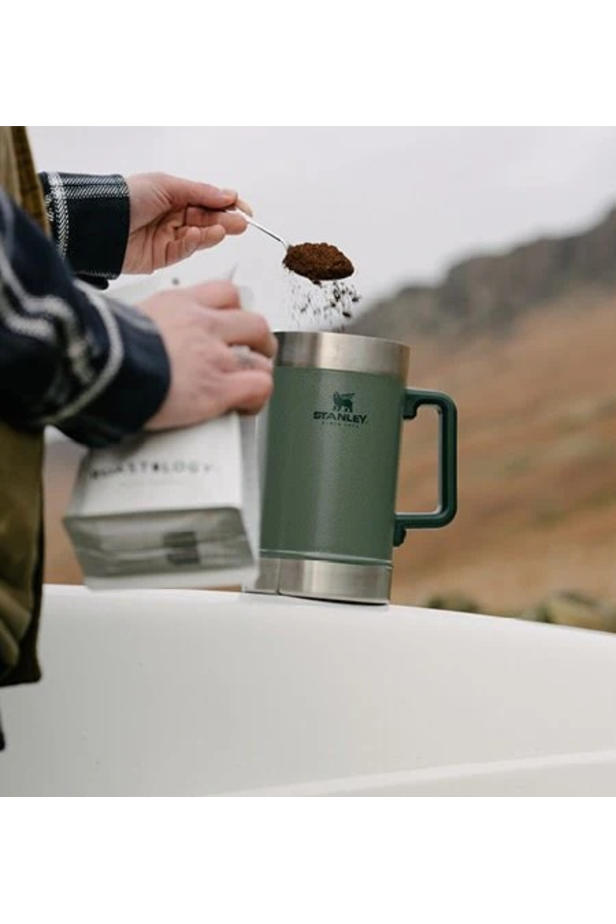 Una persona aggiunge caffè macinato da un cucchiaio in una tazza verde.