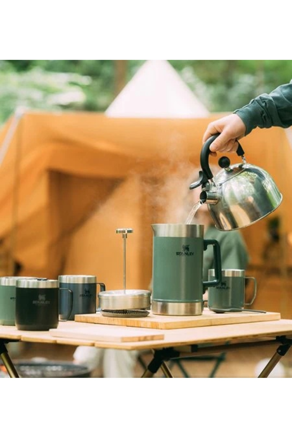Versare acqua calda da un bollitore in una caraffa verde Stanley all'aperto.