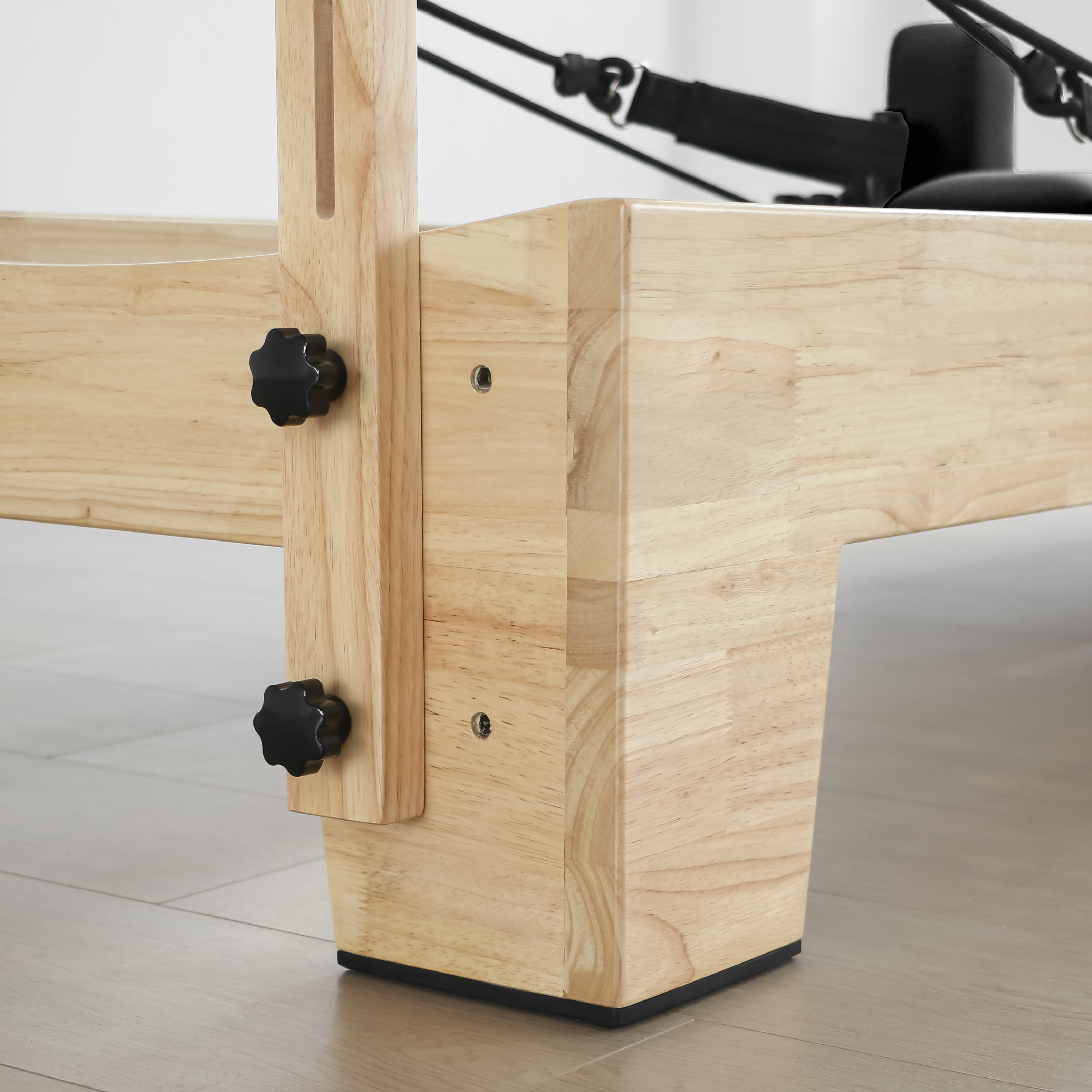 Nahaufnahme eines Holzrahmens mit schwarzen Drehknöpfen und einem Teil eines Pilatesgeräts.