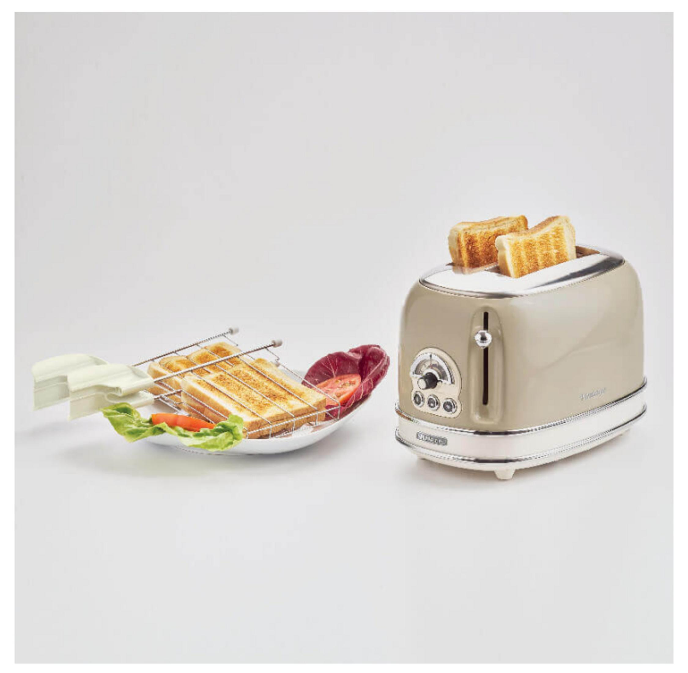 Een beige broodrooster met twee sneetjes toast en een mandje met toast, sla en tomaat.