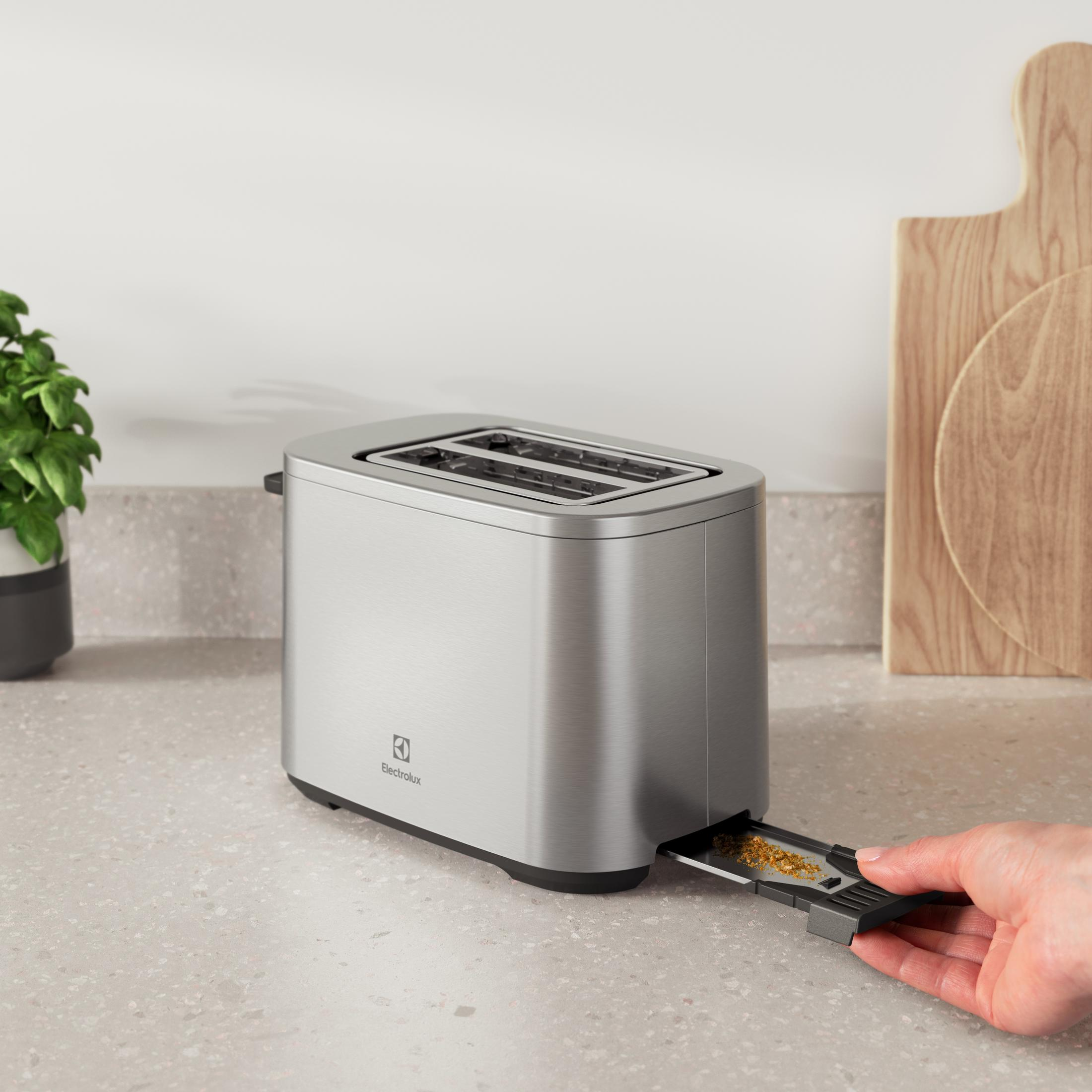 Ein silberner Toaster steht auf einer Arbeitsplatte, eine Hand zieht die Krümelschublade heraus.