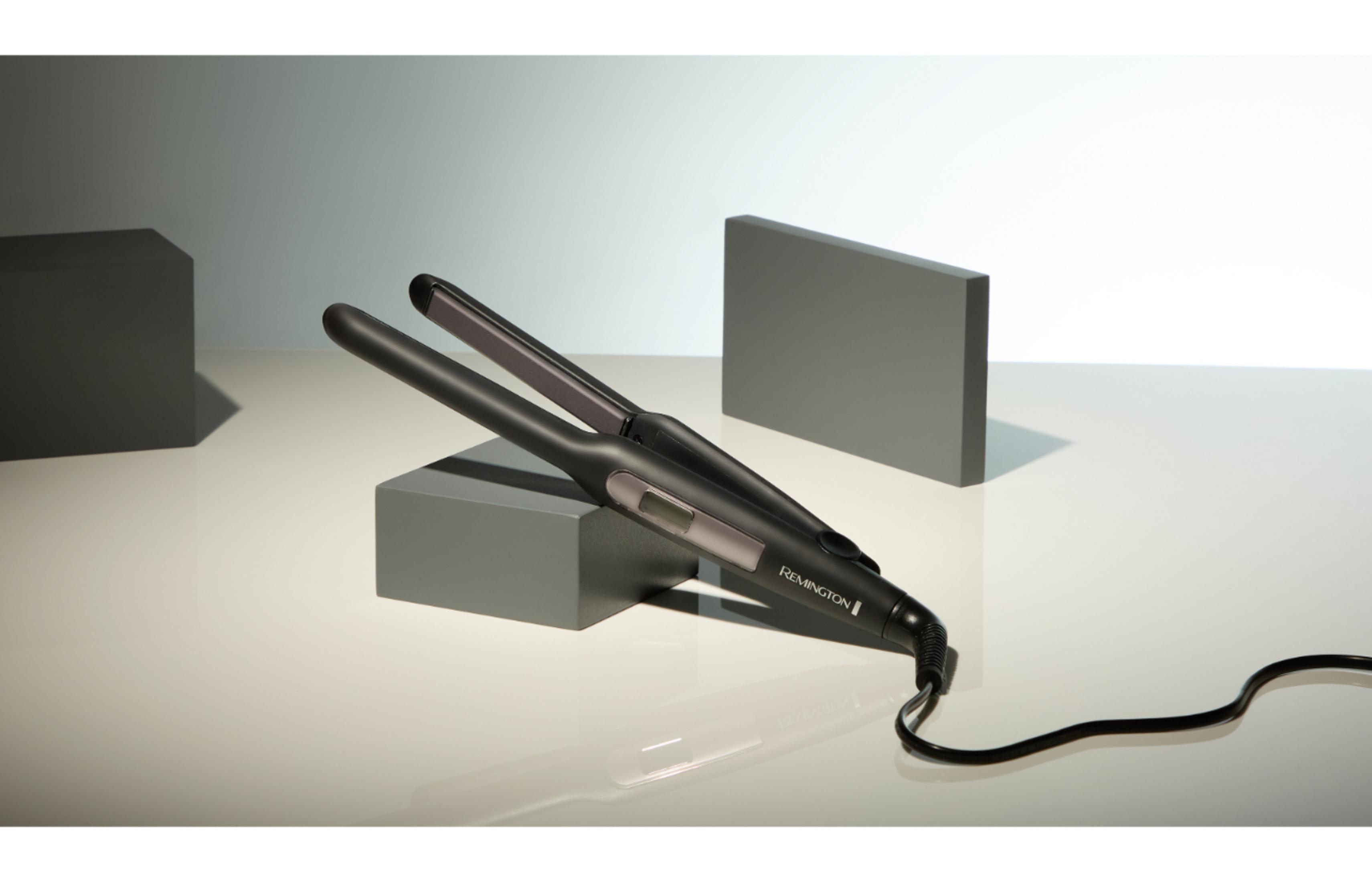 Czarna prostownica Remington leży na szarych blokach na jasnym tle.