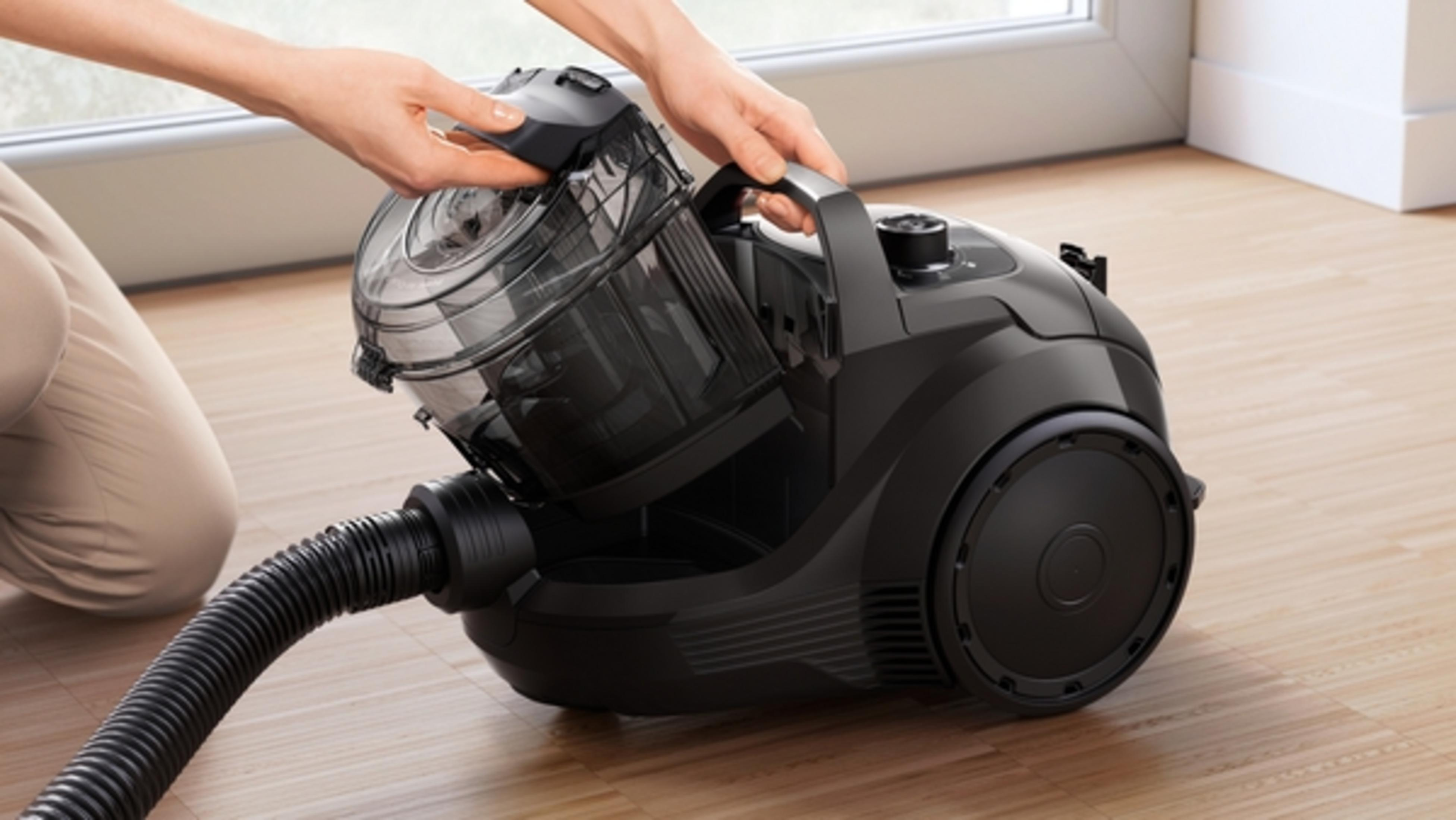Osoba otwiera pojemnik na kurz czarnego odkurzacza na drewnianej podłodze.