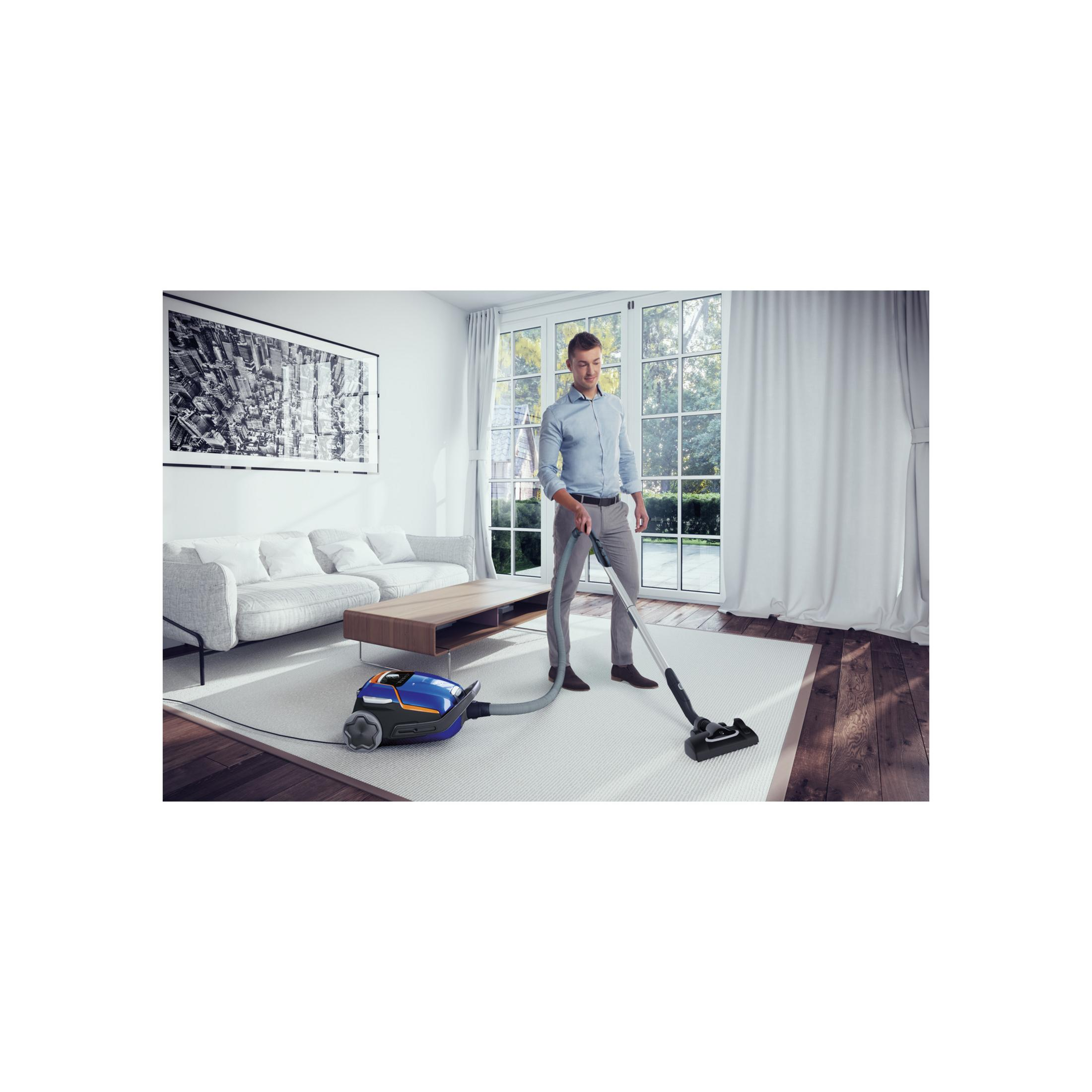 Hombre aspira alfombra en sala luminosa con sofá y ventana.