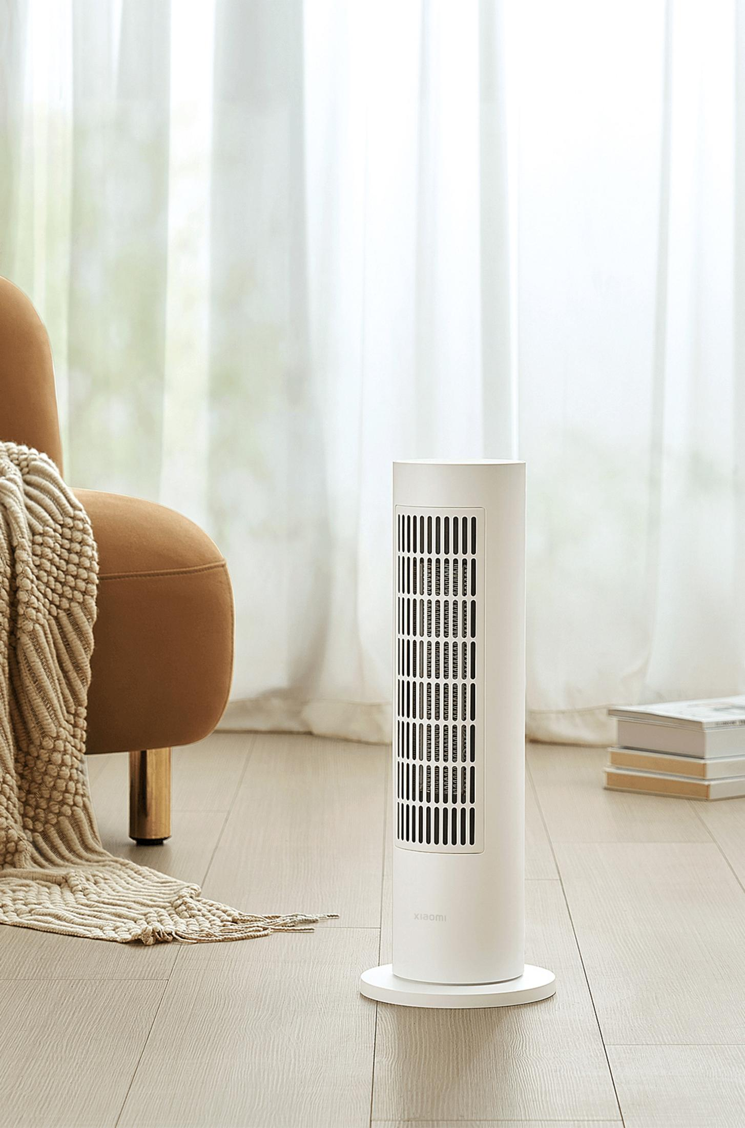 Biały wentylator wieżowy stoi na drewnianej podłodze obok brązowego fotela.