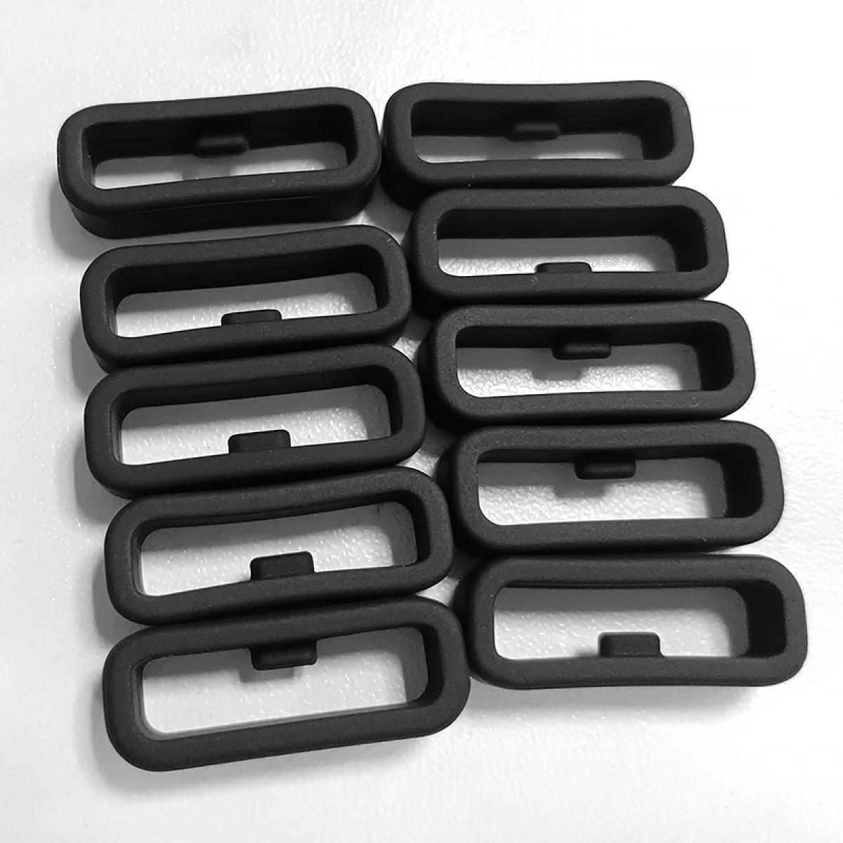 Dziesięć czarnych, prostokątnych pętli silikonowych leży na białej powierzchni.