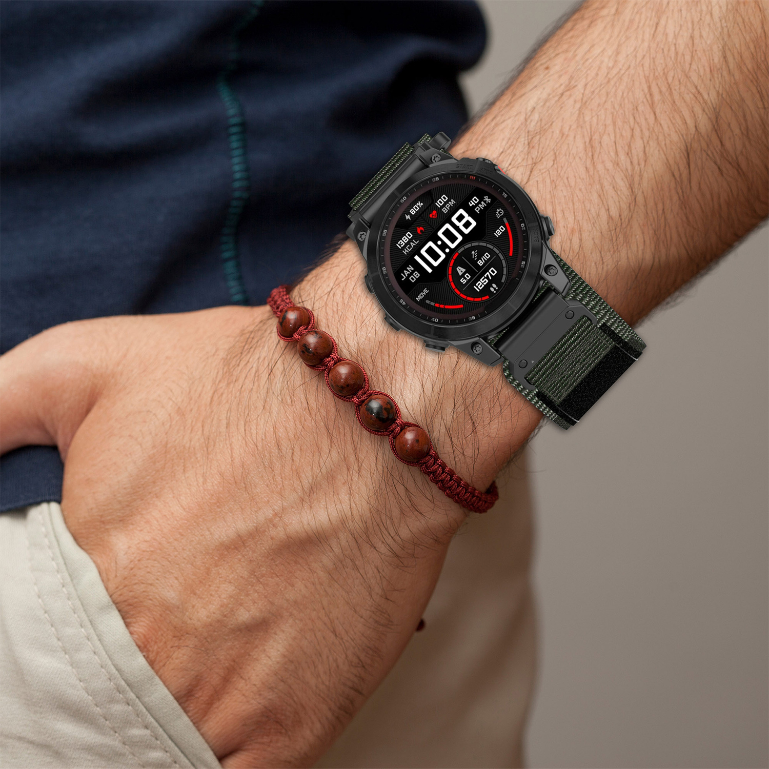 Ein Männerhandgelenk zeigt eine schwarze Smartwatch mit grünem Band und Perlenarmband.