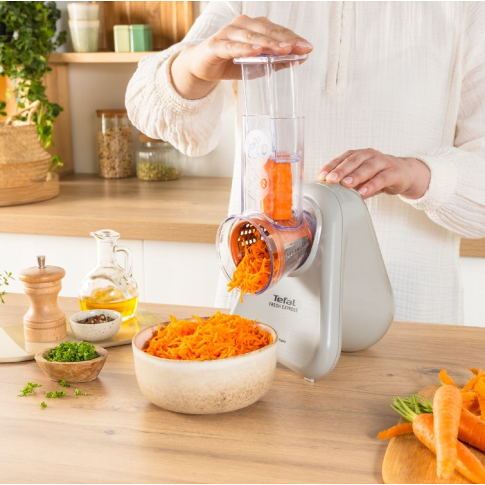 Osoba trze marchewki za pomocą urządzenia kuchennego. Starte marchewki w misce.