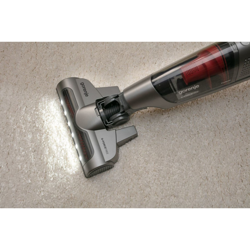 Szara głowica odkurzacza z podświetleniem świeci na jasnym dywanie.