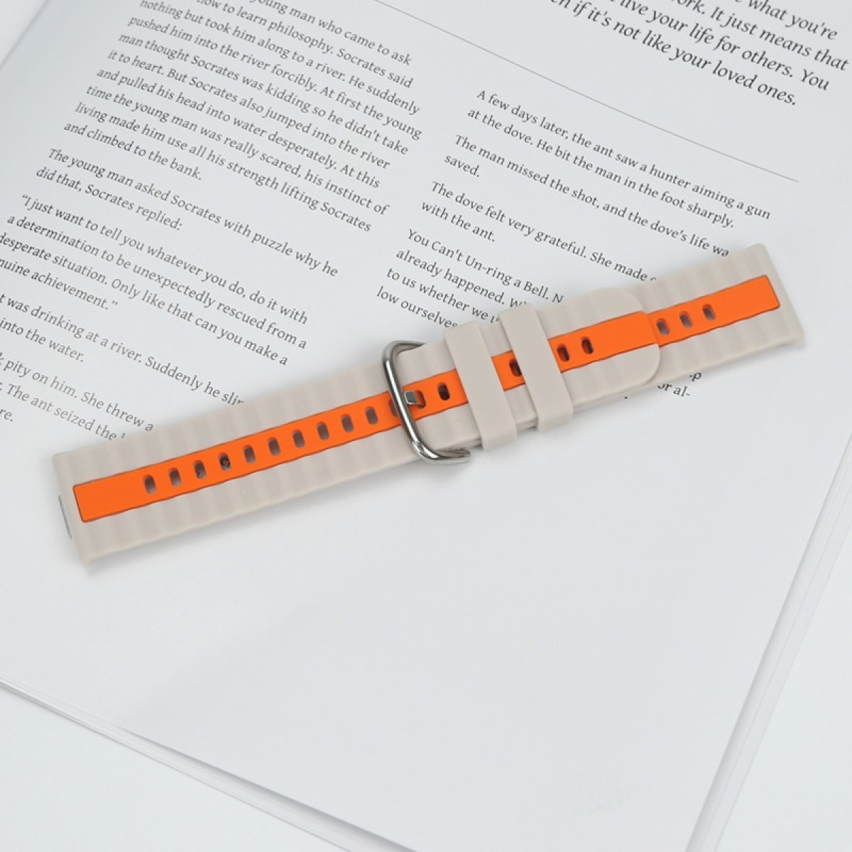 Ein beigefarbener Uhrenarmband mit orangefarbenen Akzenten liegt auf geöffneten Büchern.