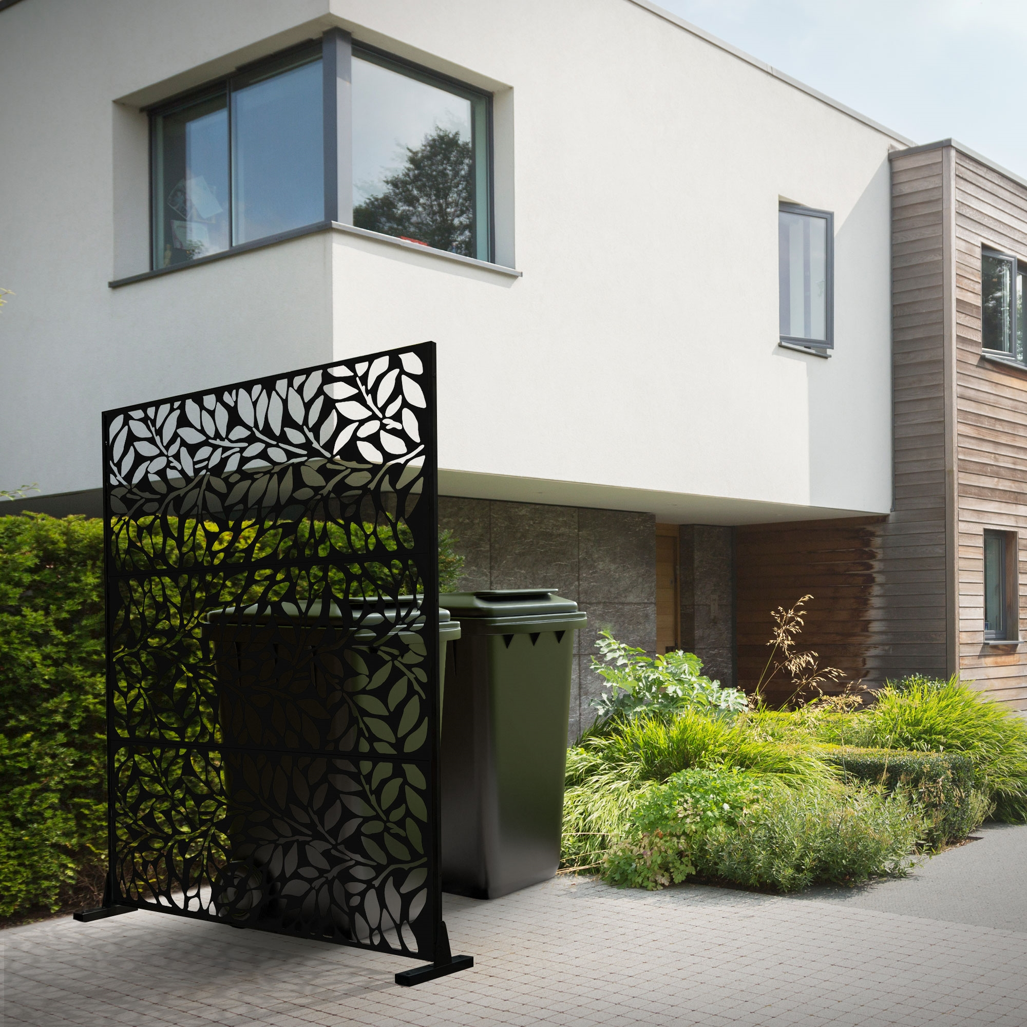 Schwarzer Sichtschutz mit Blattmuster vor grünen Mülltonnen und Haus.
