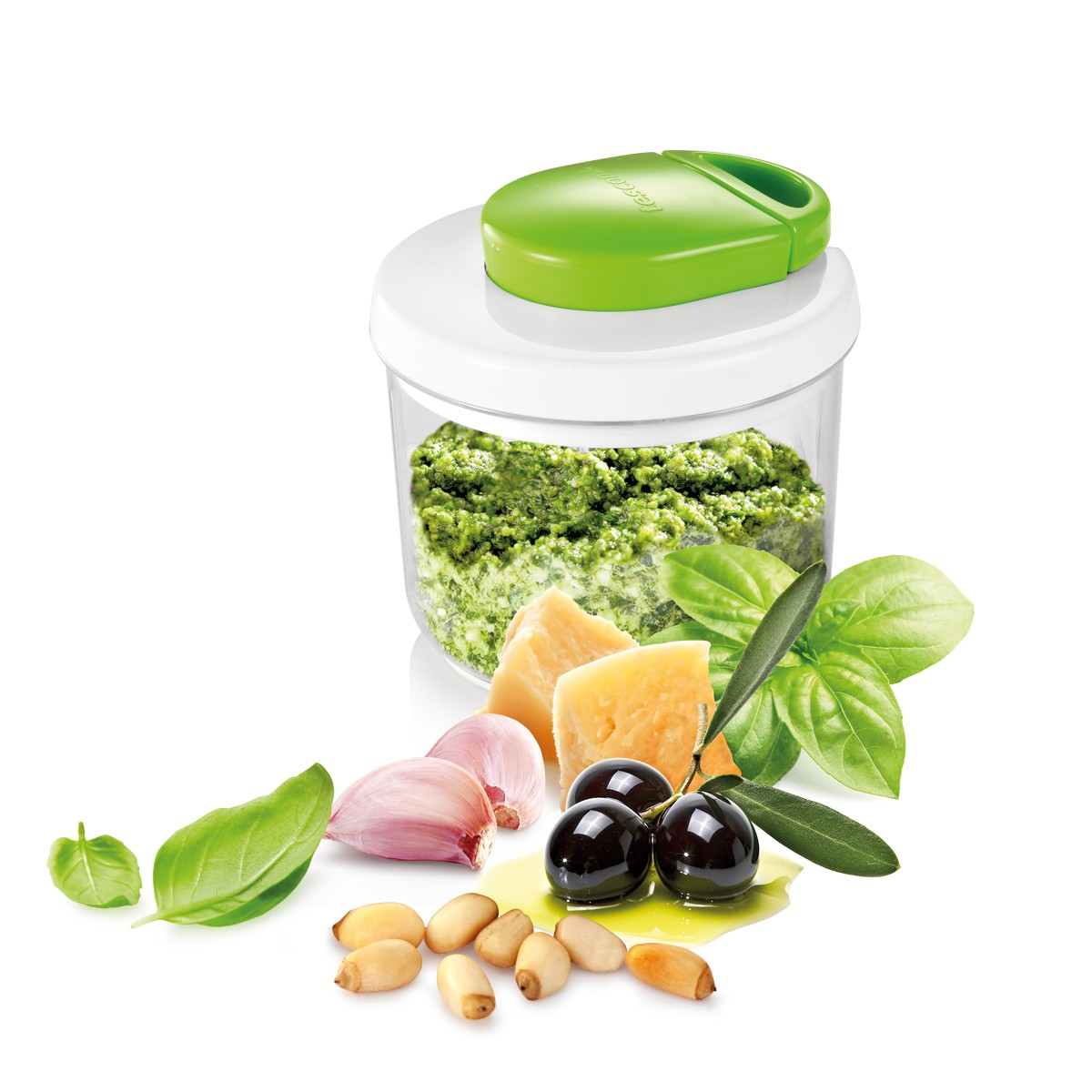 Ein grüner manueller Zerkleinerer mit Pesto, daneben Zutaten wie Knoblauch, Pinienkerne, Oliven und Basilikum.