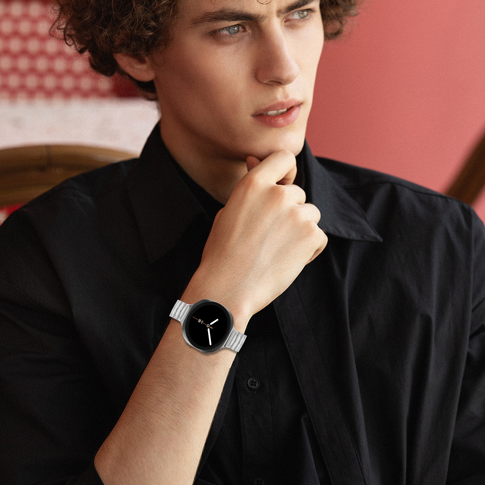 Ein Mann mit lockigem Haar trägt ein schwarzes Hemd und eine silberne Uhr.