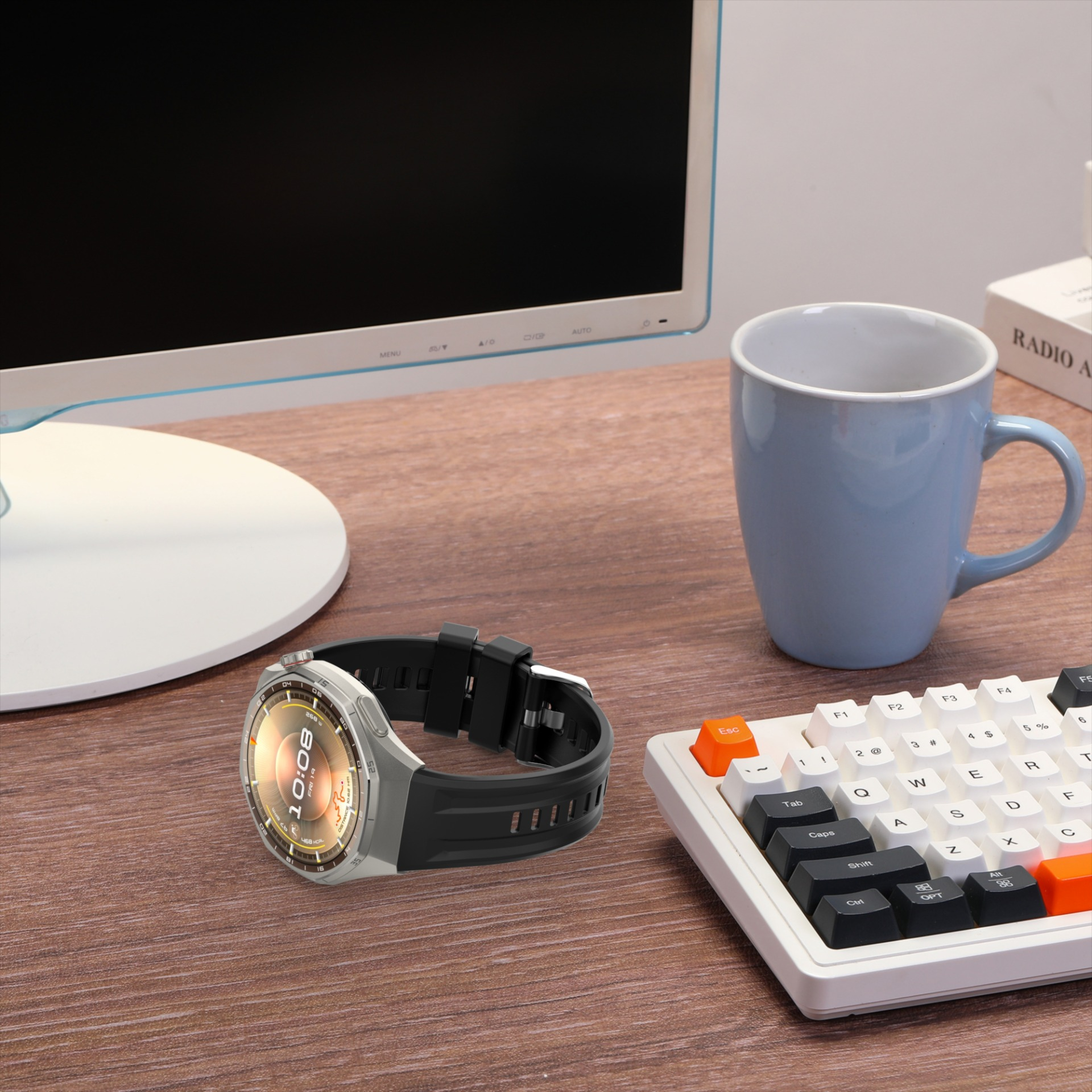 Silberne Smartwatch mit schwarzem Armband auf einem Schreibtisch neben einer blauen Tasse.