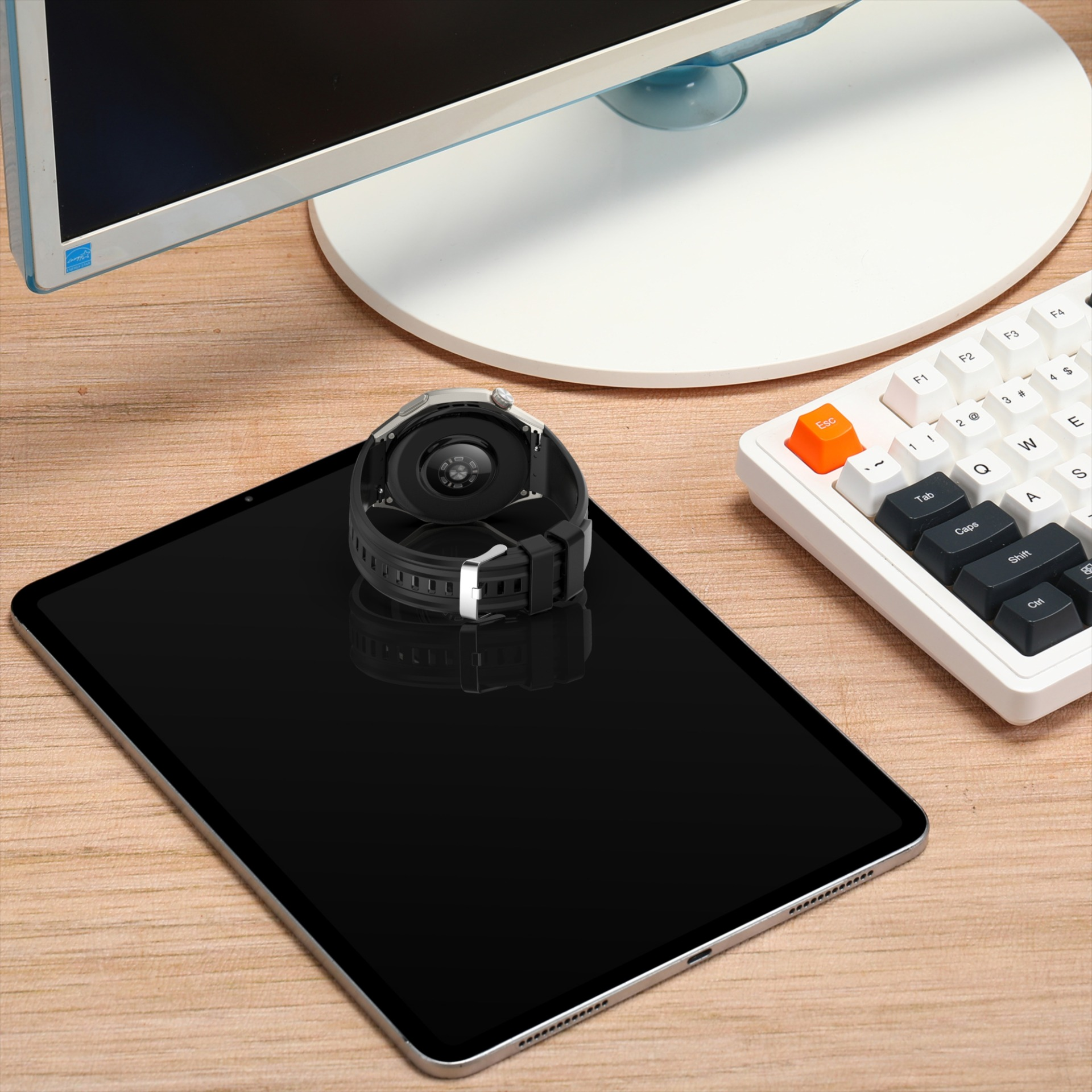 Eine Smartwatch liegt auf einem Tablet vor einem Monitor und einer Tastatur.