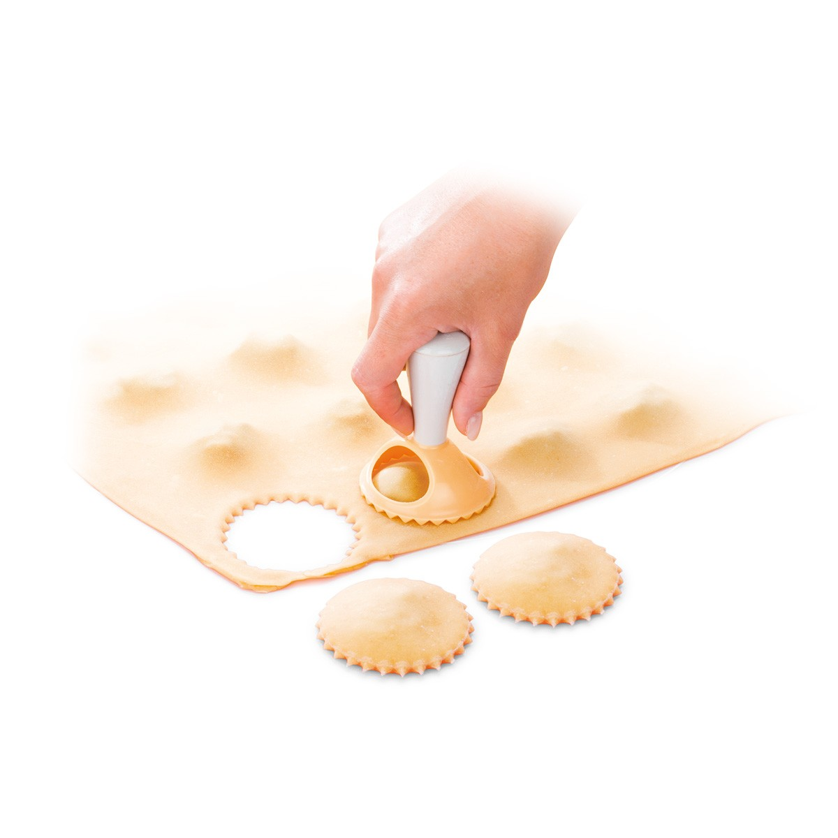 Mano con tagliapasta per ravioli su pasta. Due ravioli finiti accanto.