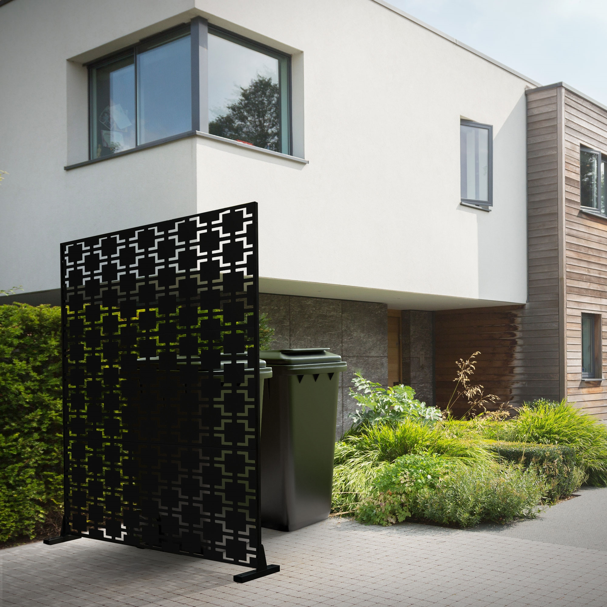 Schwarzer Sichtschutz mit Muster vor modernem Haus mit Mülltonne.