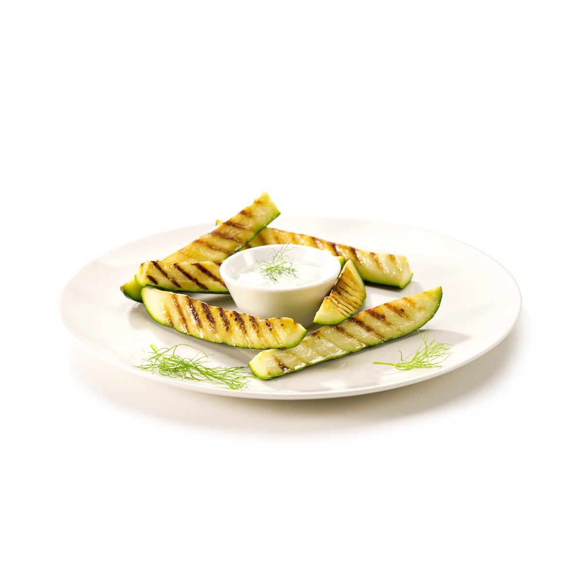 Gegrillte Zucchinischeiben um eine kleine Schale mit weißem Dip, garniert mit Dill.