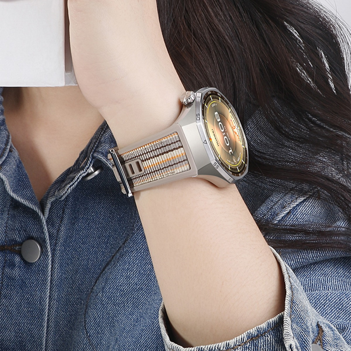 Eine Uhr mit Stoffarmband wird an einem Arm getragen, der ein Jeanshemd trägt.