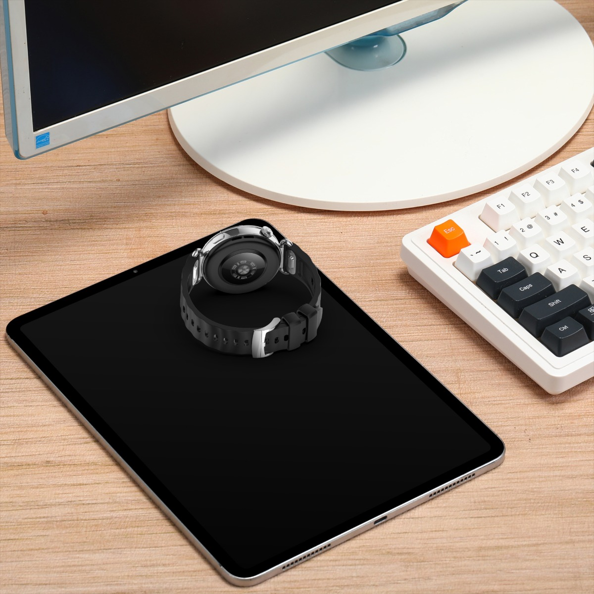 Eine Smartwatch liegt auf einem schwarzen Tablet neben Tastatur und Monitor.