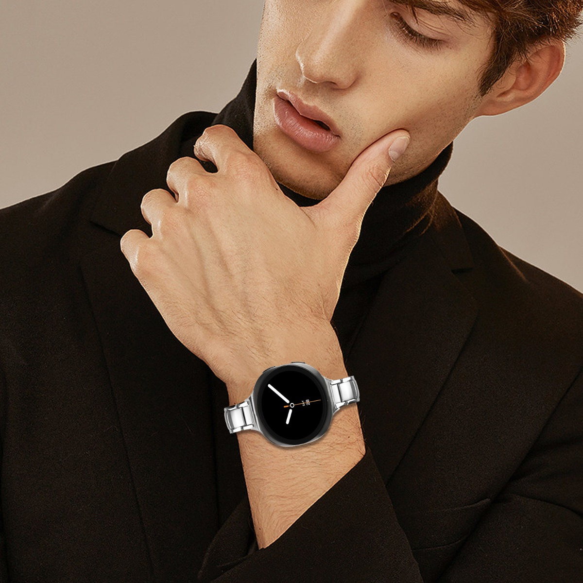 Ein Mann trägt einen schwarzen Rollkragenpullover und einen schwarzen Blazer mit einer silbernen Smartwatch am linken Handgelenk.
