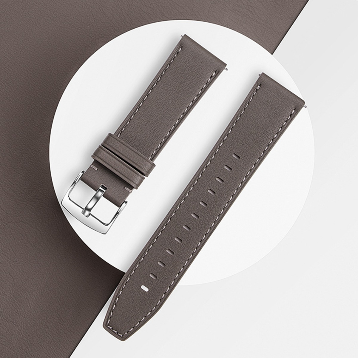 Graues Lederarmband mit silberner Schnalle und weißen Nähten, auf weißem Kreis.