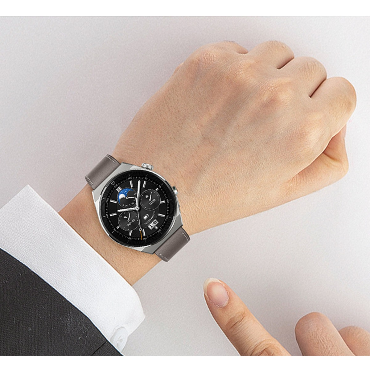 Eine Hand trägt eine Smartwatch mit grauem Armband, schwarzem Zifferblatt und Mondphasenanzeige.