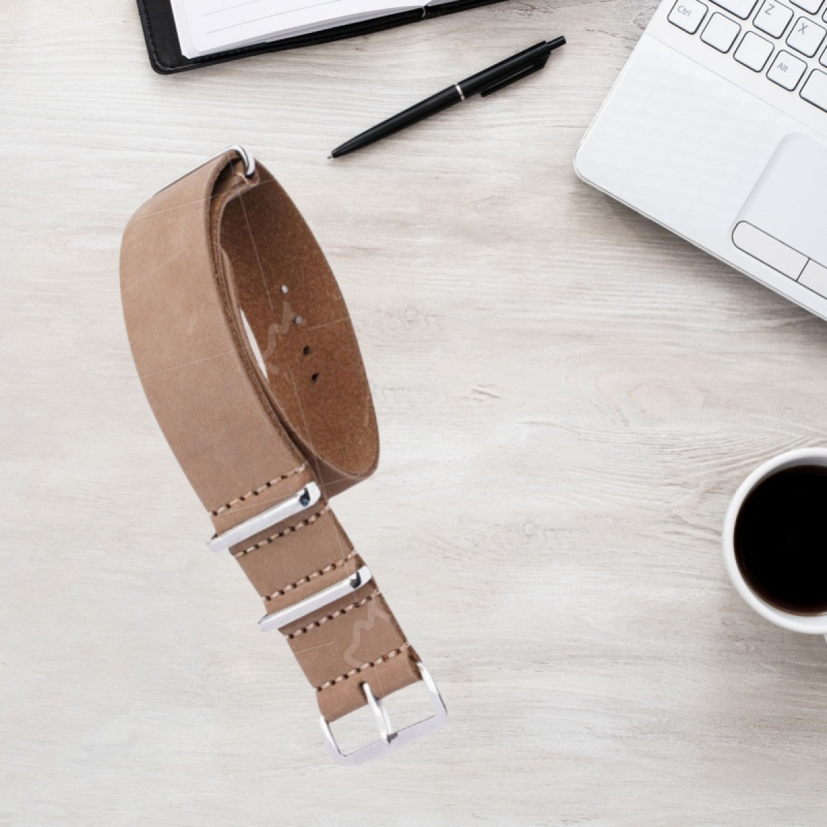 Braunes Lederarmband mit silbernen Schnallen auf einem Holztisch mit Laptop und Kaffee.