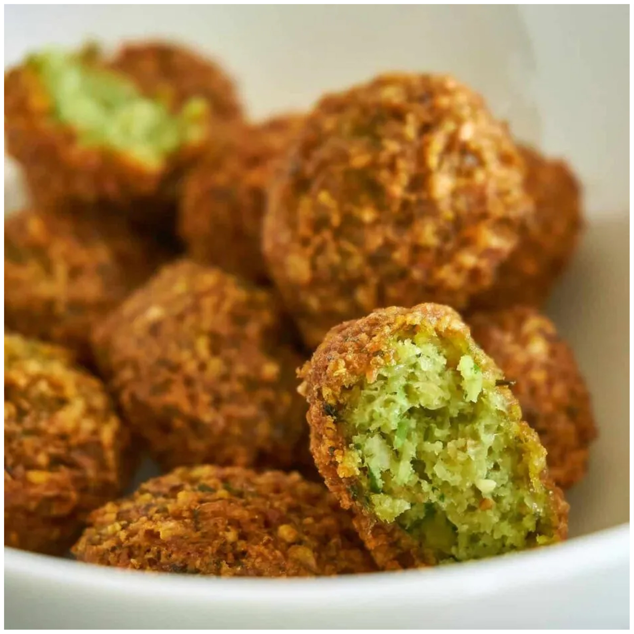 Goudbruine gefrituurde falafel in een witte kom, één is opengebroken.