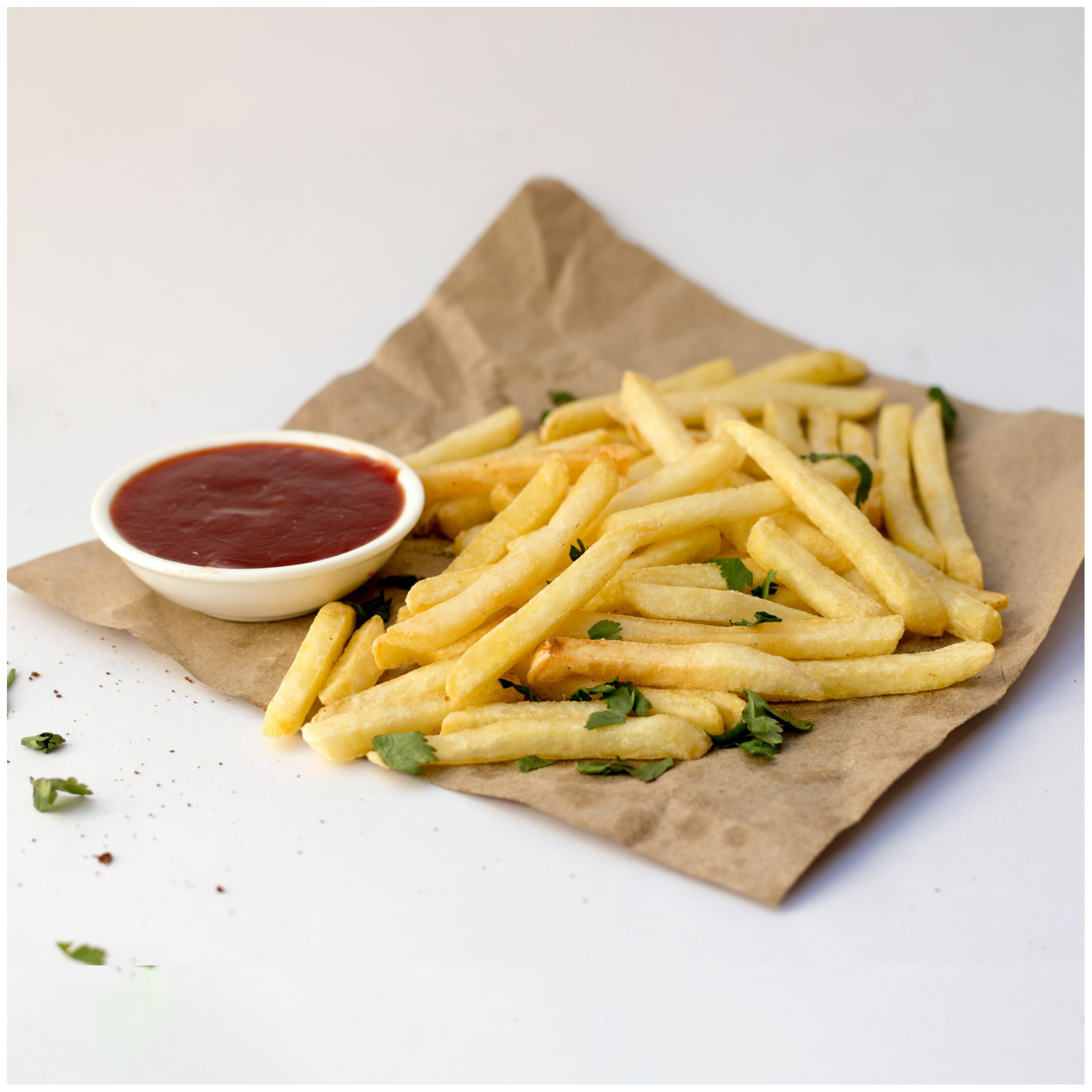 Gouden friet met peterselie en ketchup op bruin papier.