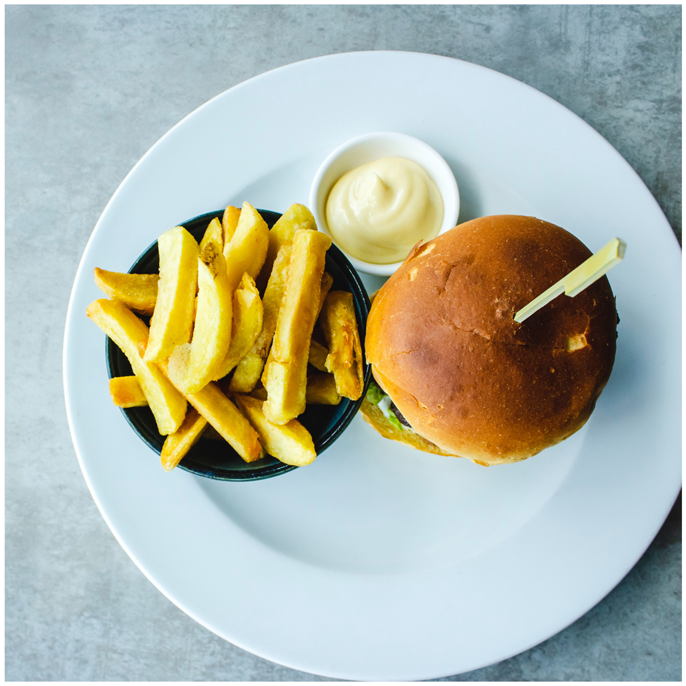 Een burger met friet en mayonaise geserveerd op een wit bord.
