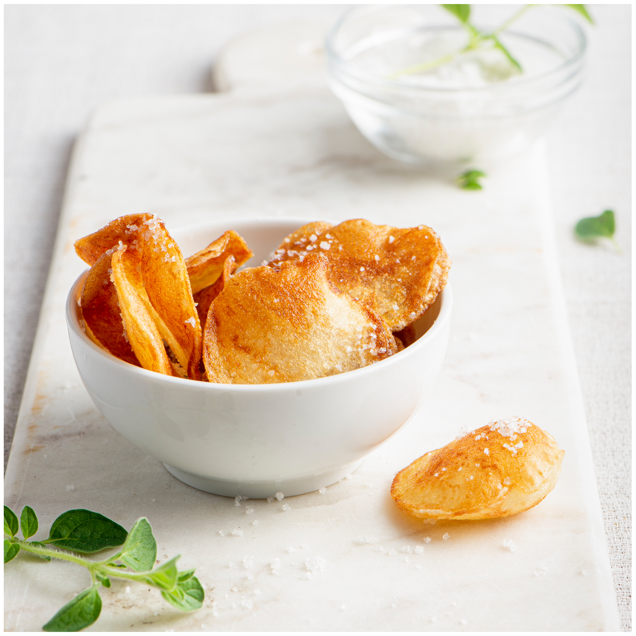 Krokante aardappelchips in een kom, bestrooid met zout, op marmeren ondergrond.