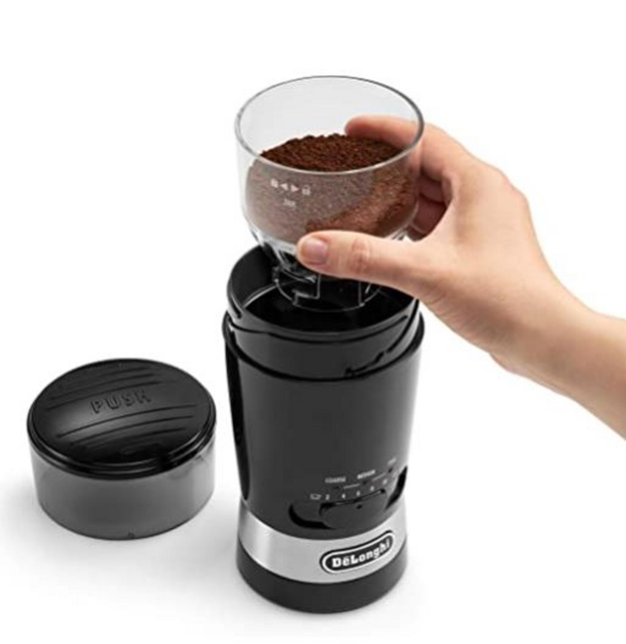 Czarny pojemnik młynka do kawy z fusami trzymany przez rękę.