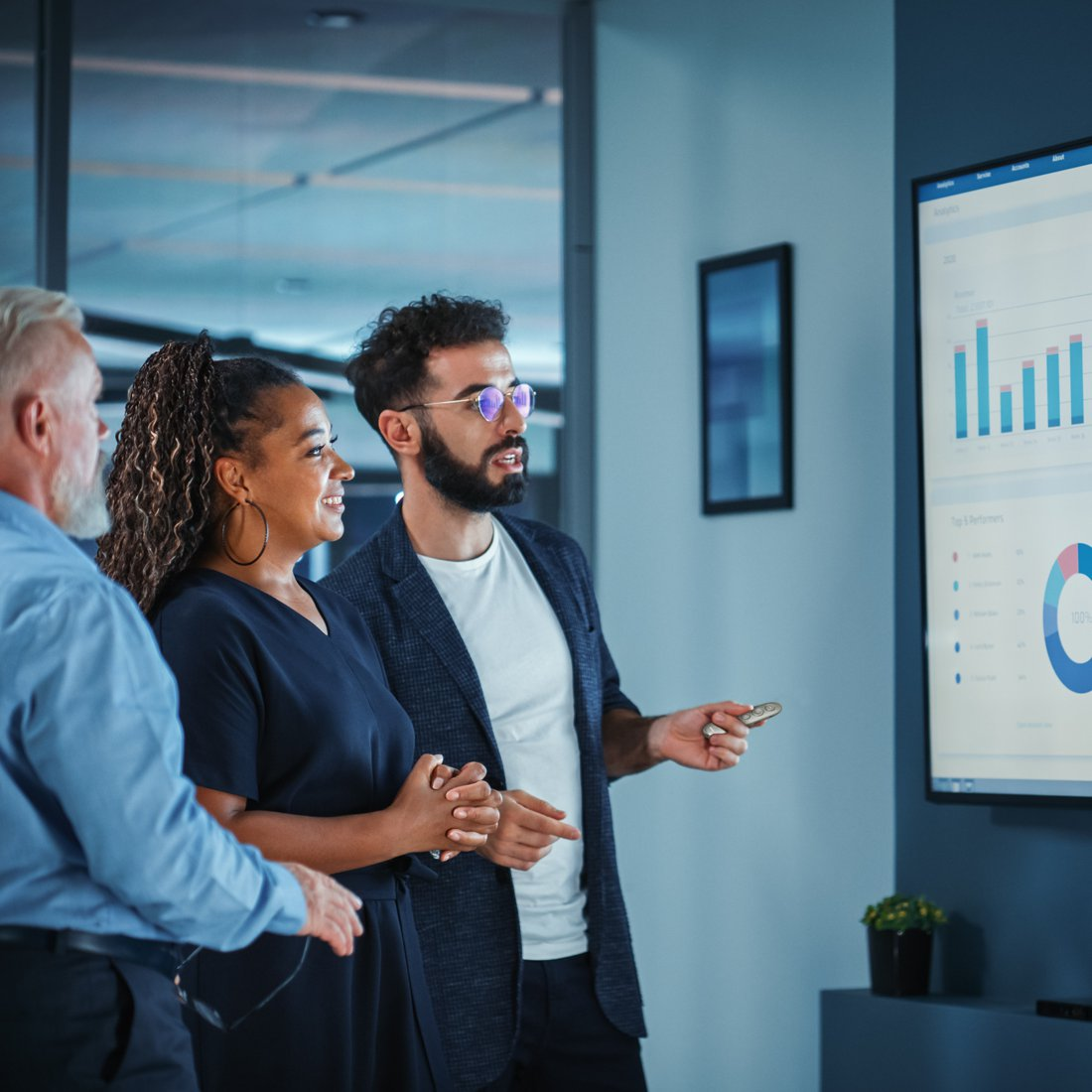 Mężczyźni i kobiety dyskutują przed ekranem z wykresami.