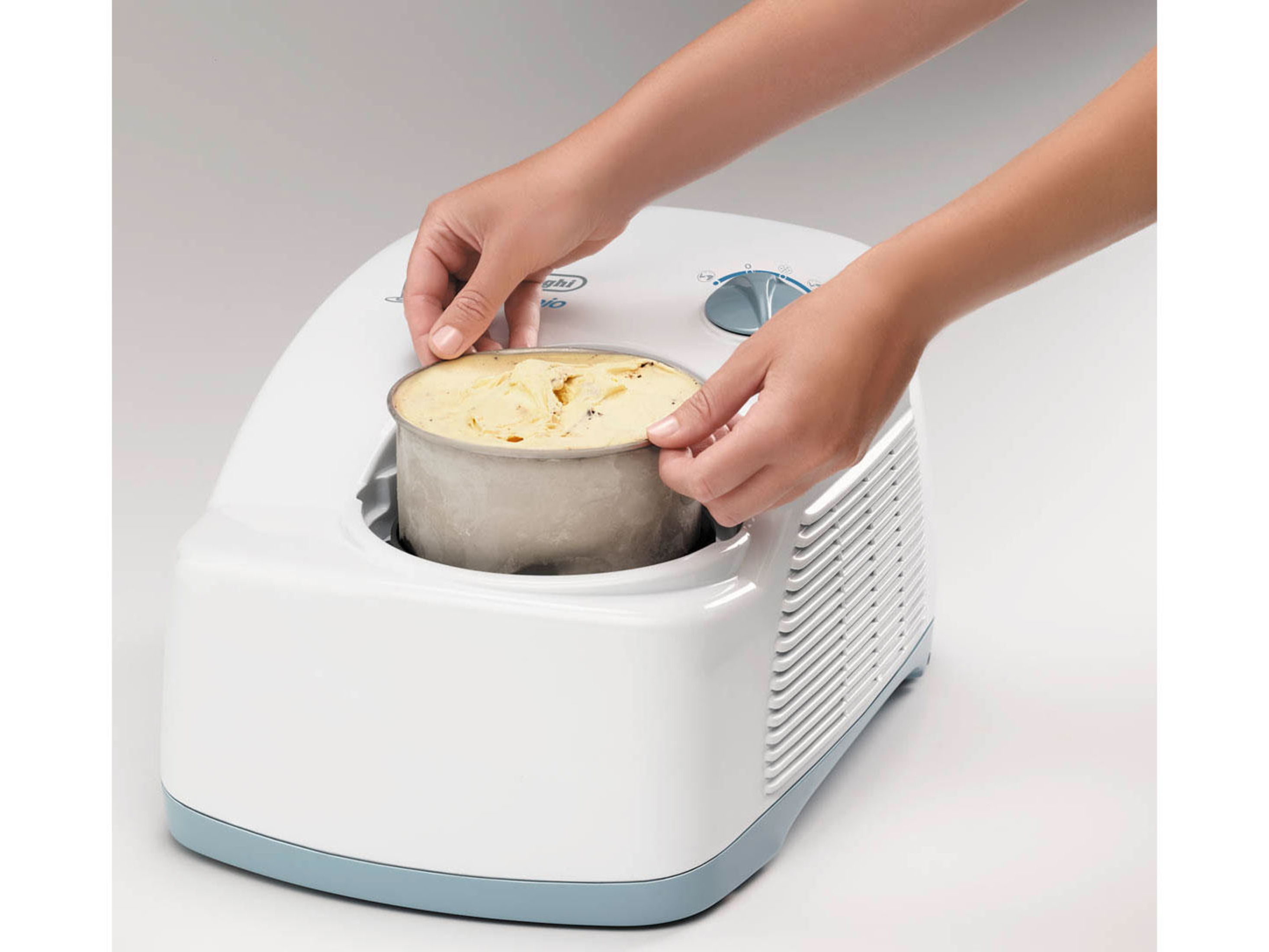 Ręce wkładają metalową miskę z lodami do białej maszyny do lodów.