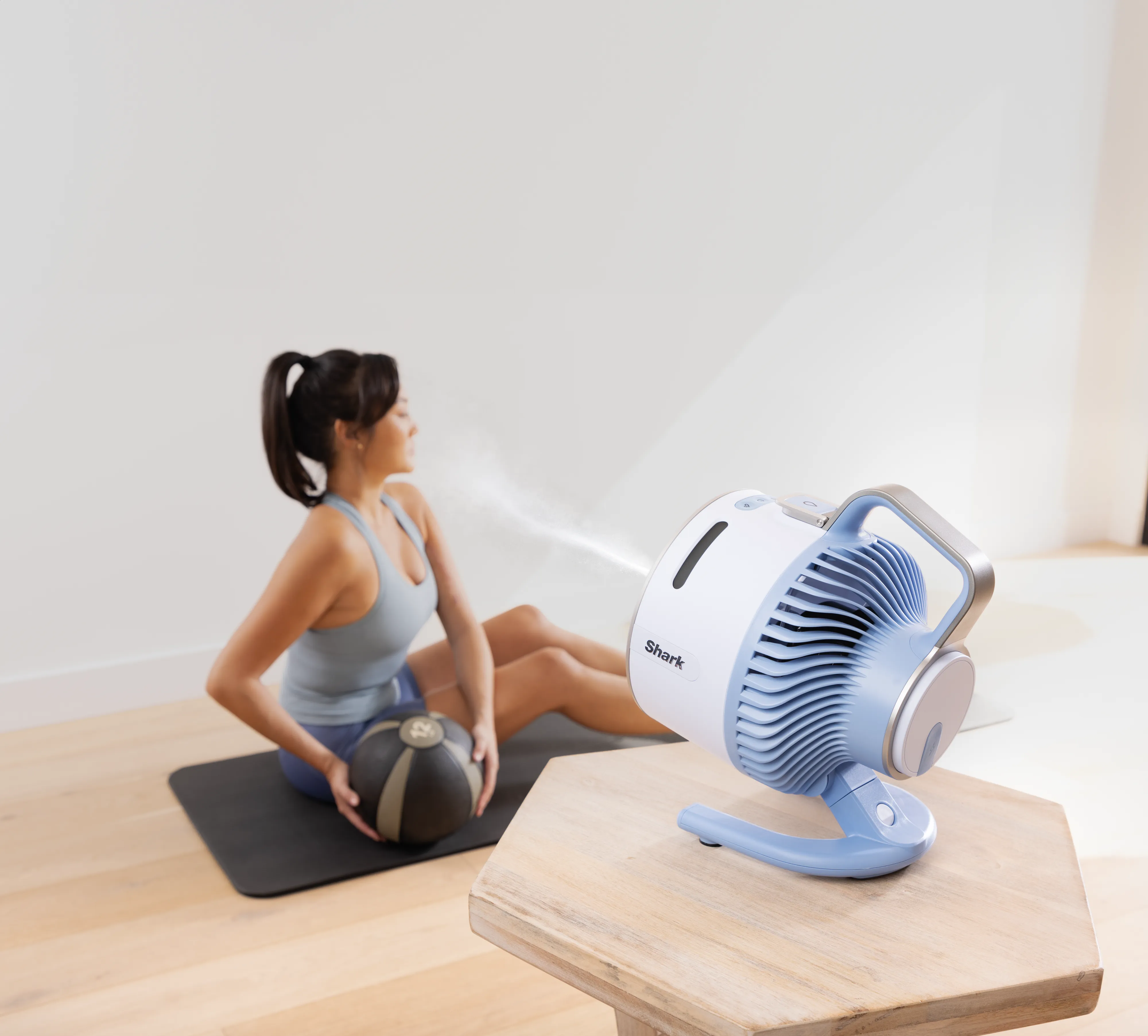 Donna su tappetino con palla medica, ventilatore spruzza nebbia.