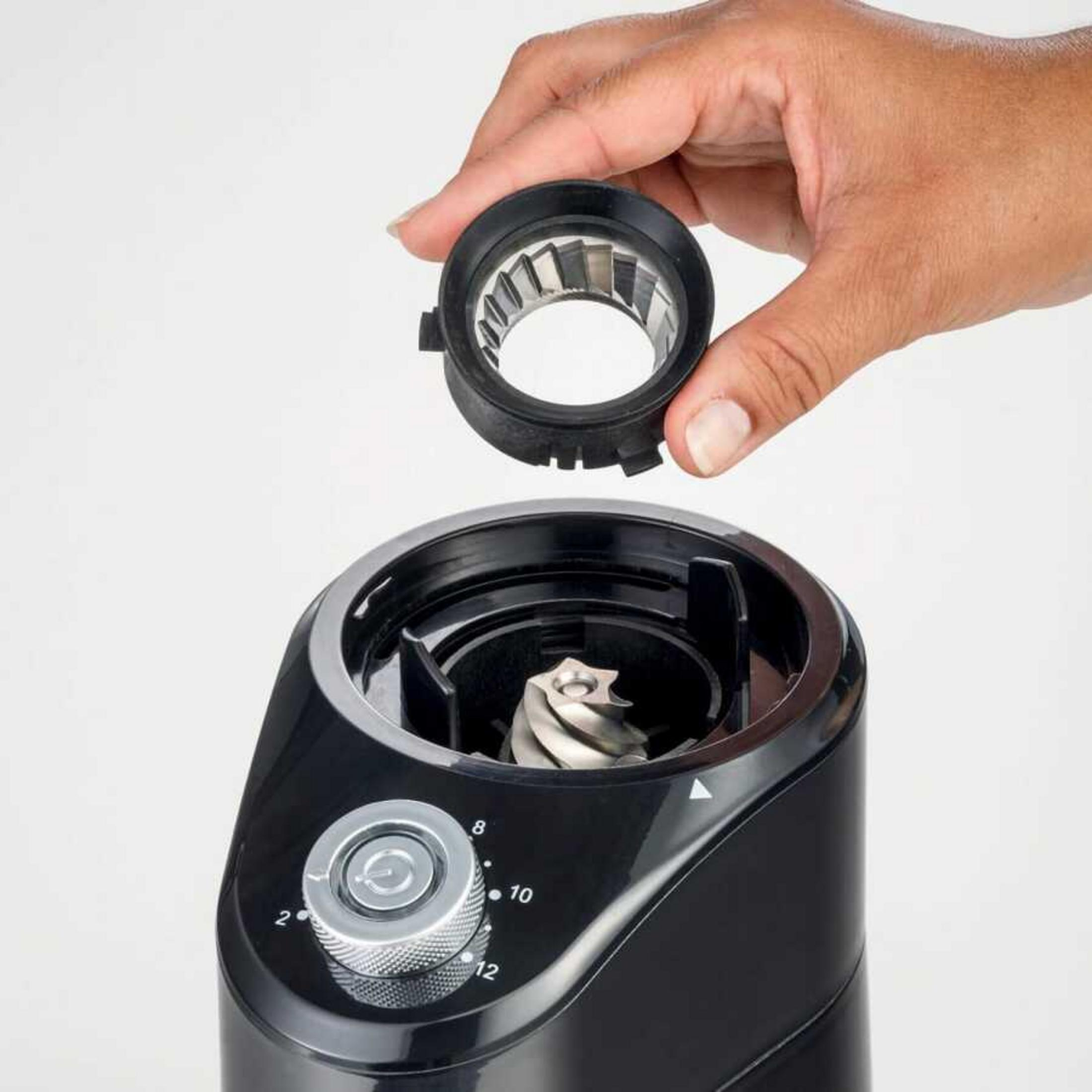 Eine Hand hält einen Mahlwerk-Einstellring über einem schwarzen Kaffeemühle.