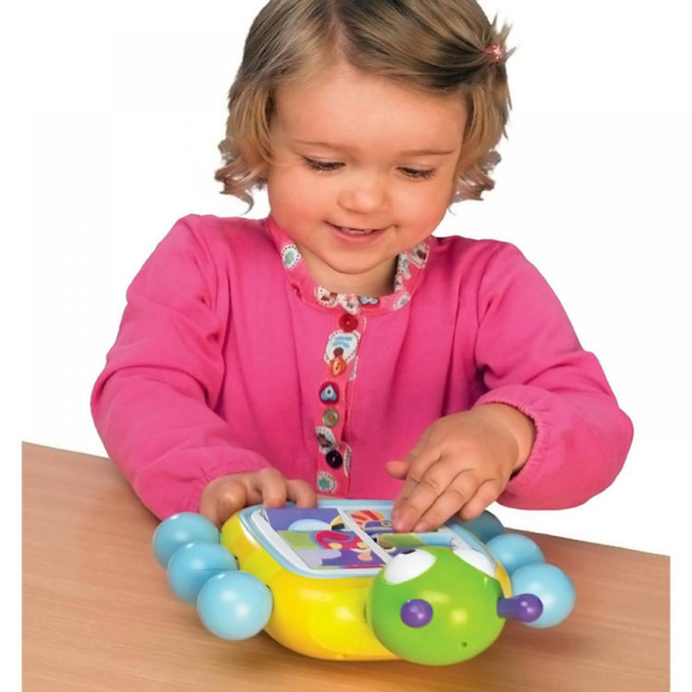 Dziewczynka w różowej bluzce bawi się kolorową zabawką gąsienicą na stole.