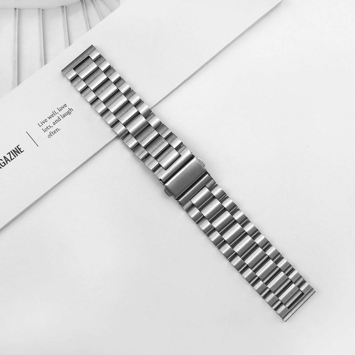Ein silbernes Metallarmband liegt auf einer Zeitschrift mit Text.
