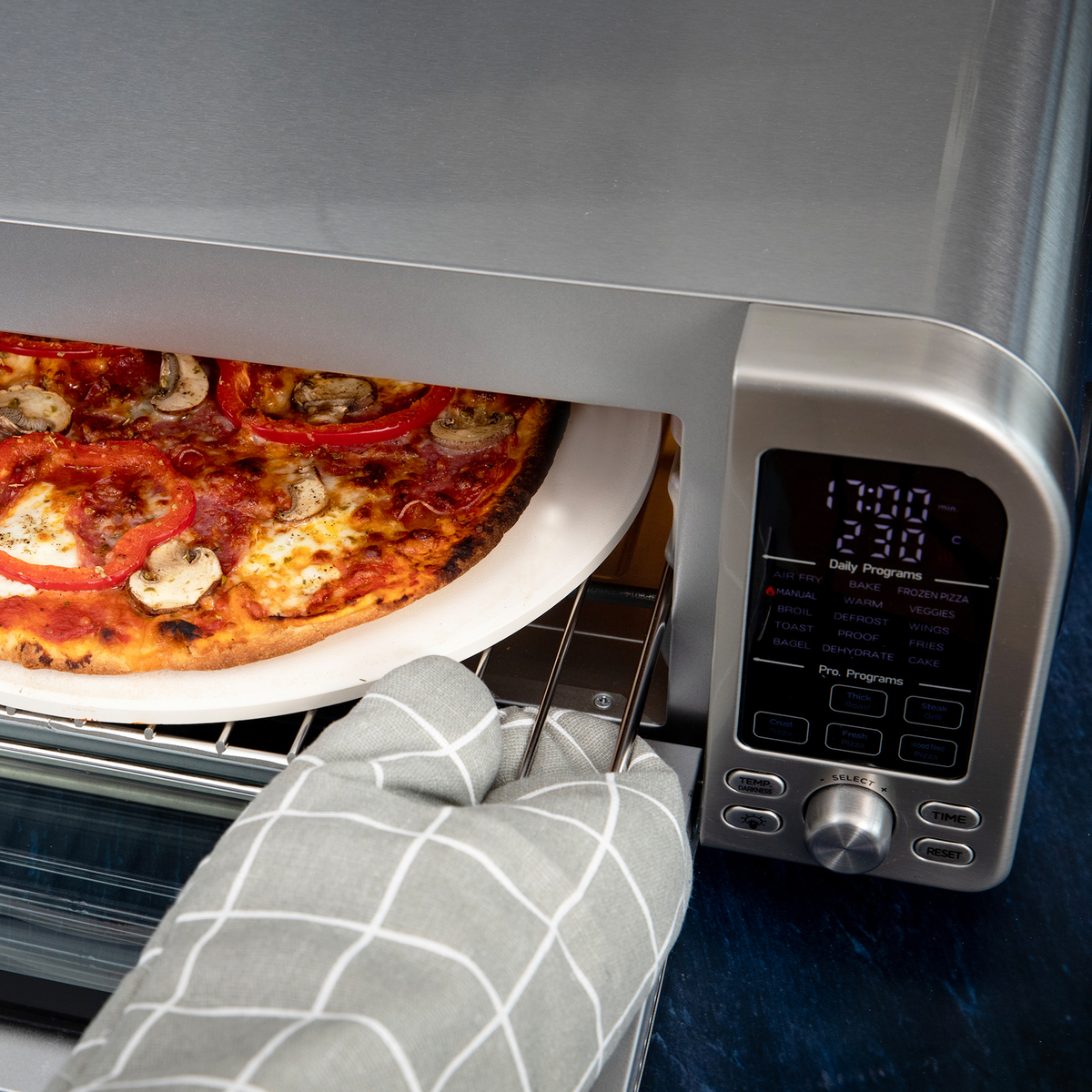 Pizza jest wyjmowana z piekarnika tostera za pomocą rękawicy kuchennej.