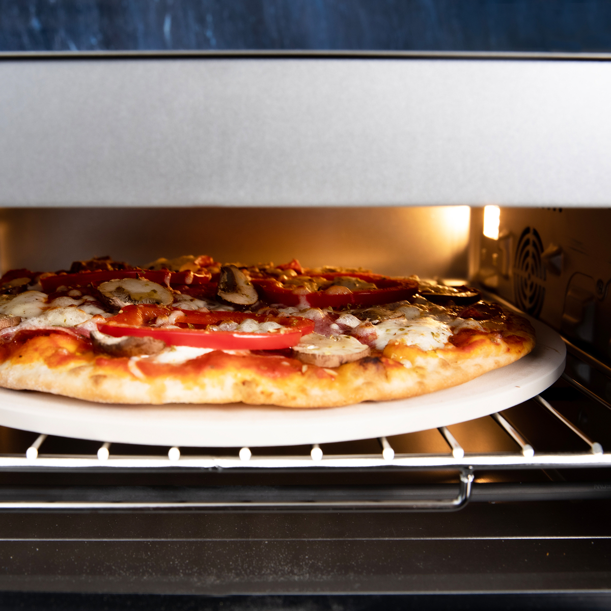 Pizza z grzybami i pomidorami piecze się w piekarniku na kamieniu do pizzy.