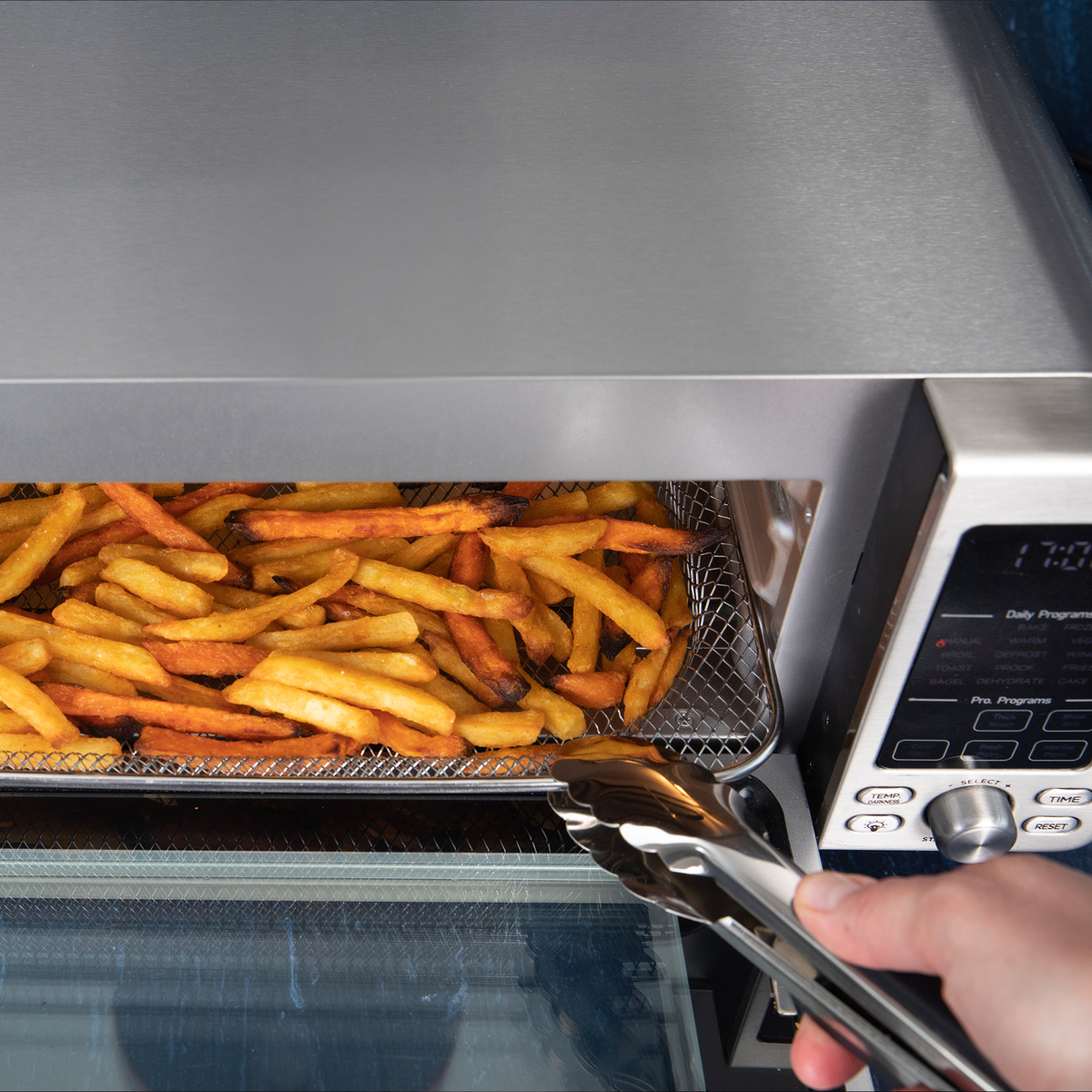 Złociste frytki w koszyku frytkownicy beztłuszczowej wyjmowane szczypcami.