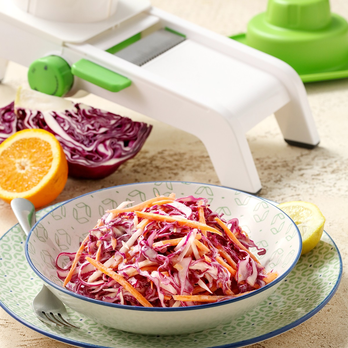 Ein Schüsselchen Coleslaw neben roten Kohl, Orange und Zitrone mit einem Hobel.