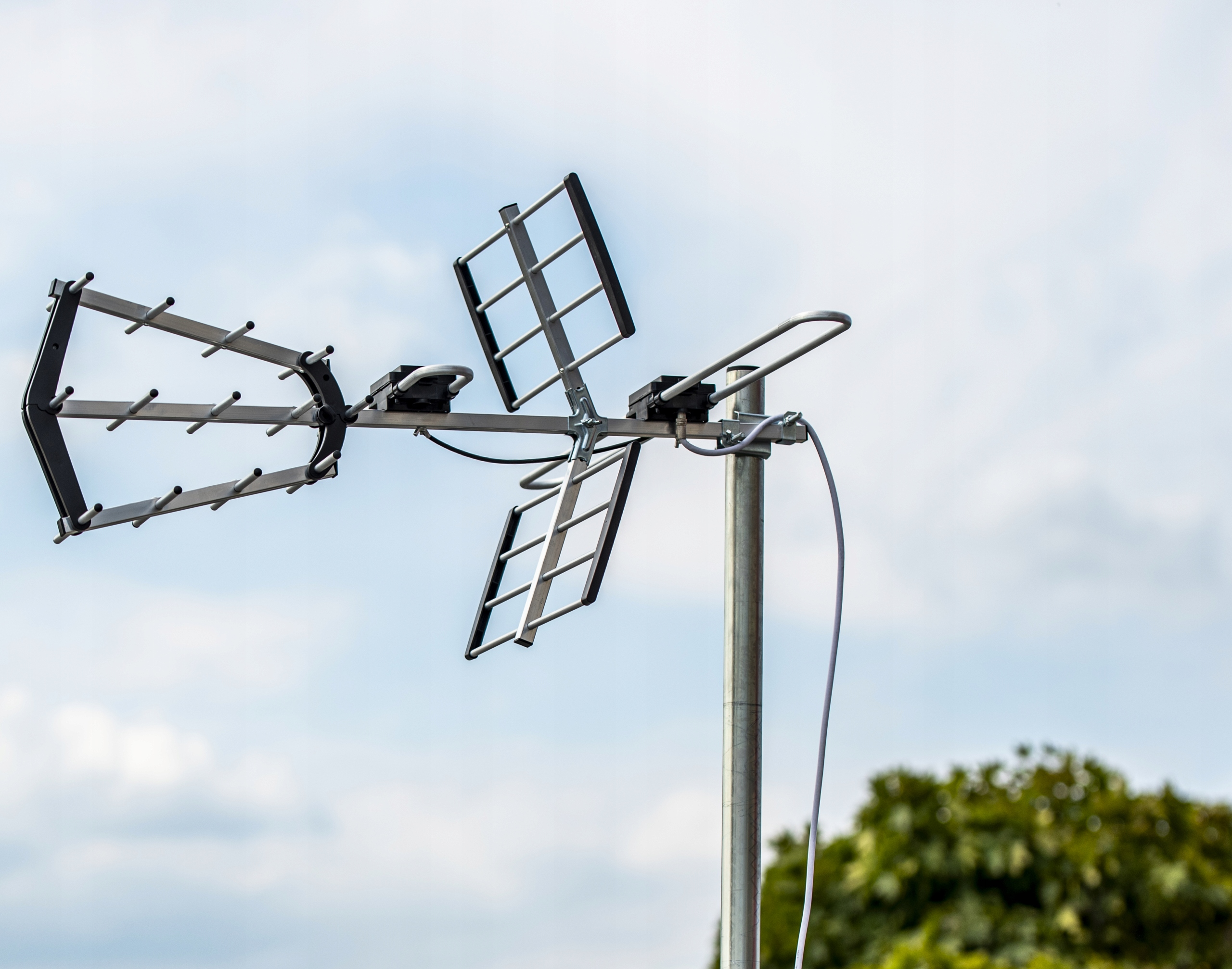 Antena telewizyjna wieloelementowa przymocowana do masztu na tle pochmurnego nieba.