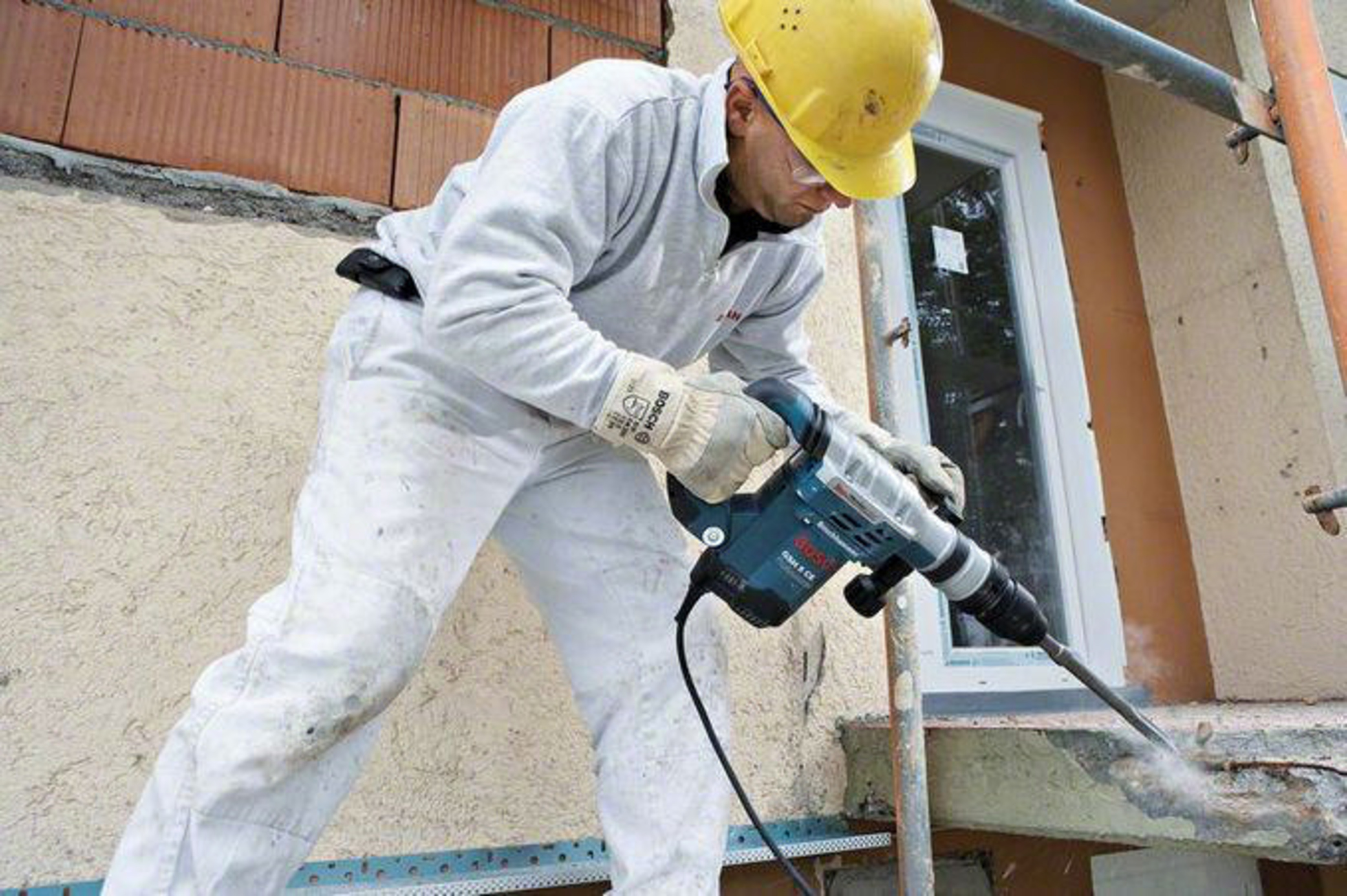 Obrero de construcción con casco amarillo usa martillo percutor en pared.