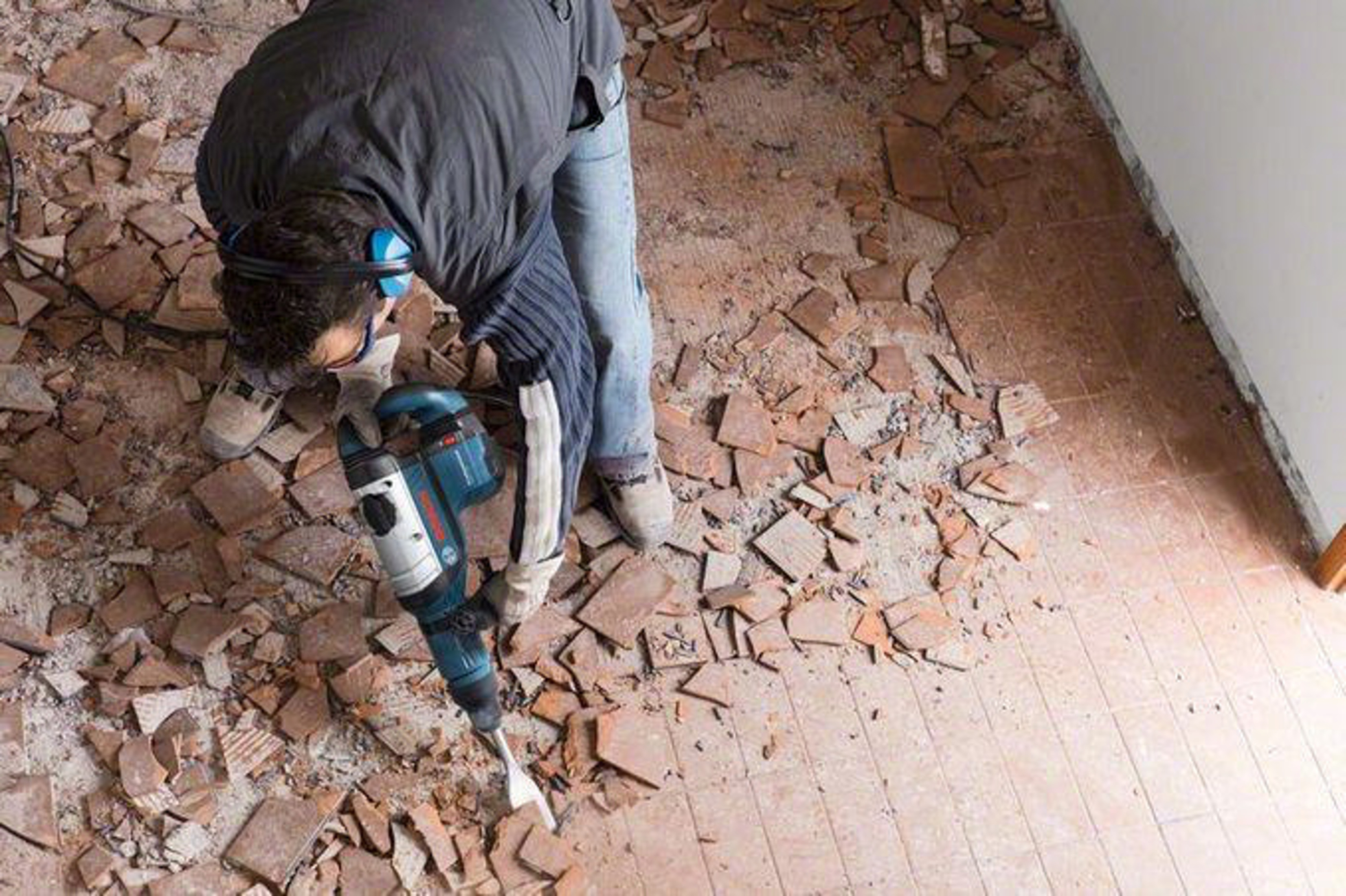 Un uomo con un martello pneumatico rimuove vecchie piastrelle.