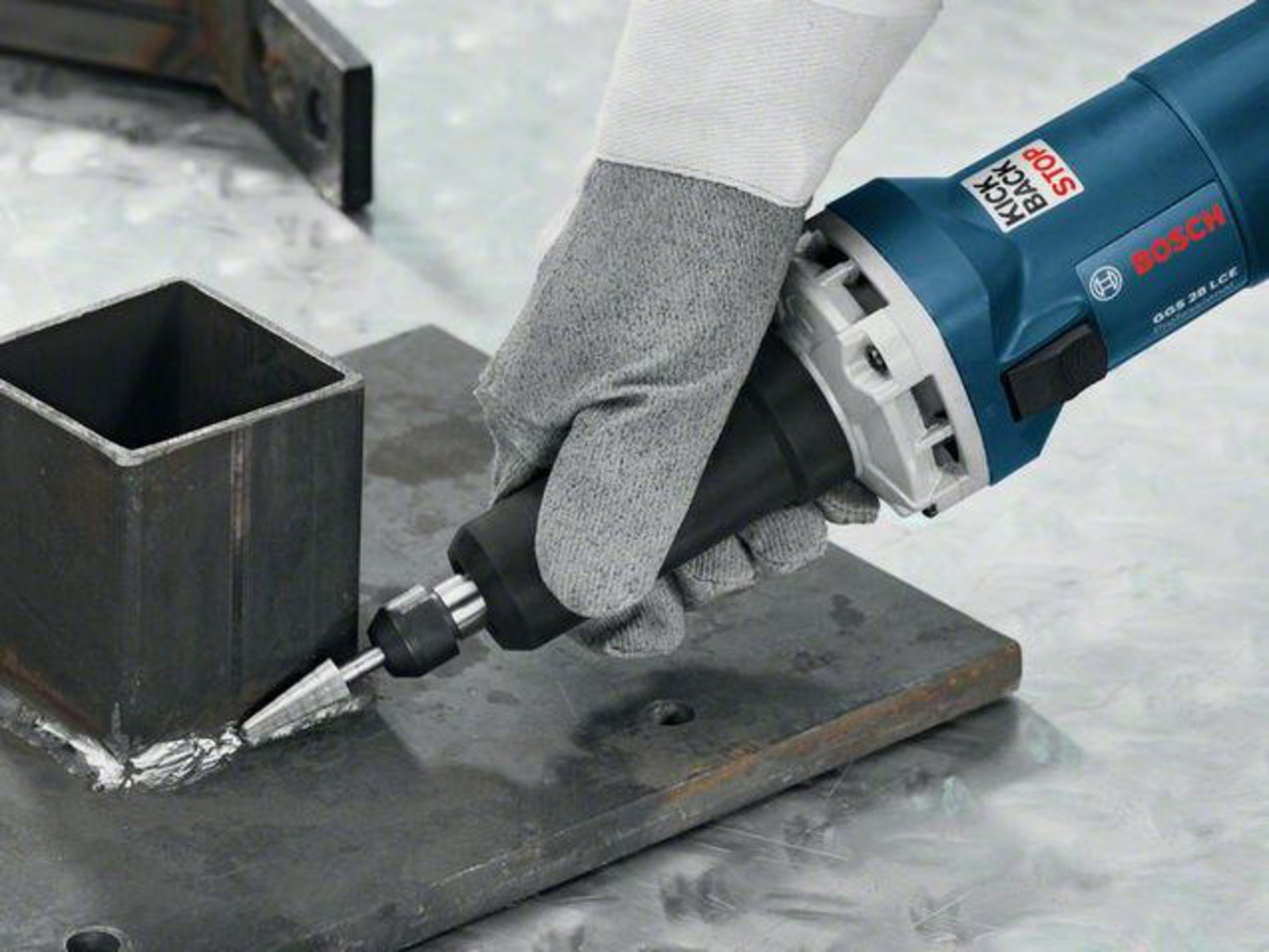 Una mano enguantada usa una amoladora Bosch azul en piezas de metal.