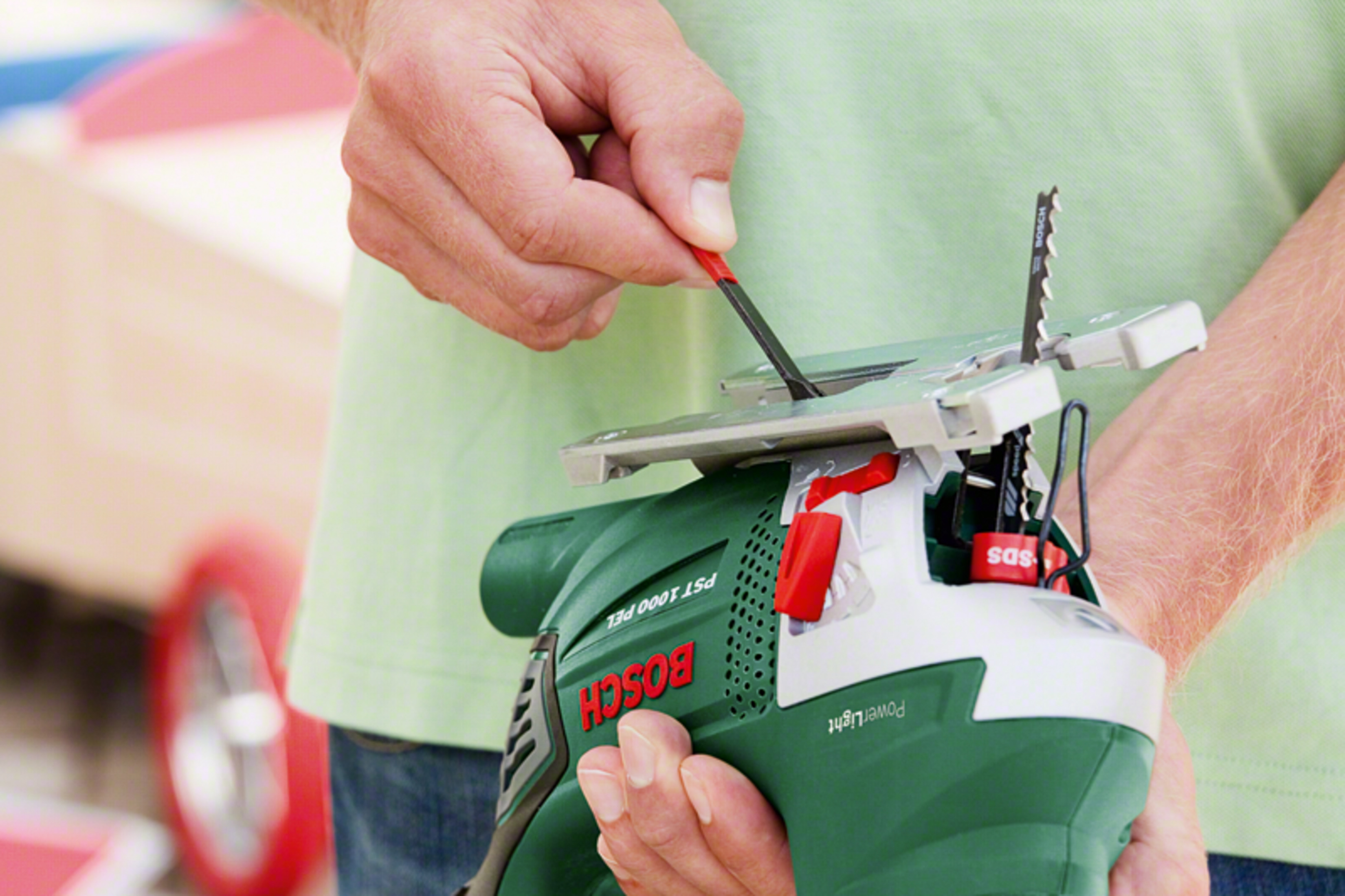 Bir kişi yeşil bir Bosch dekupaj testeresi tutuyor ve bıçağı takıyor.